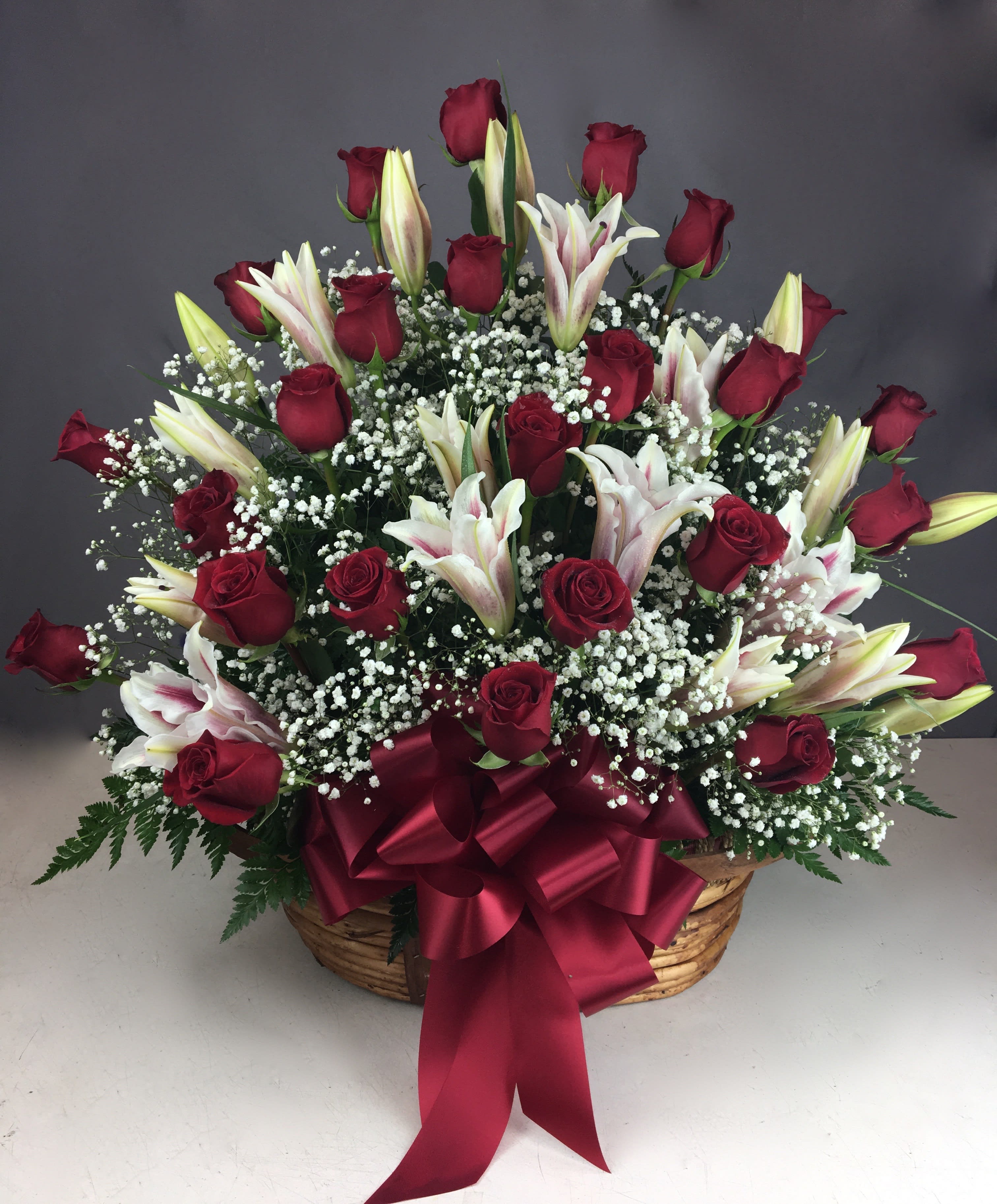 Basket arrangement of red roses and white lilies with a burgundy ribbon