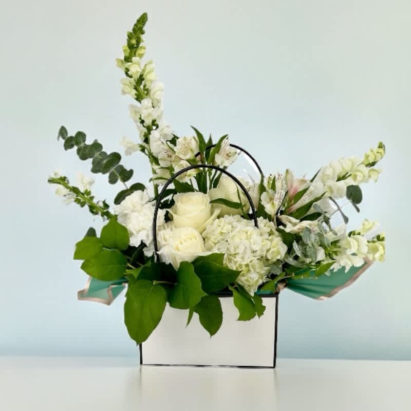 White floral arrangement in a white box with black handles