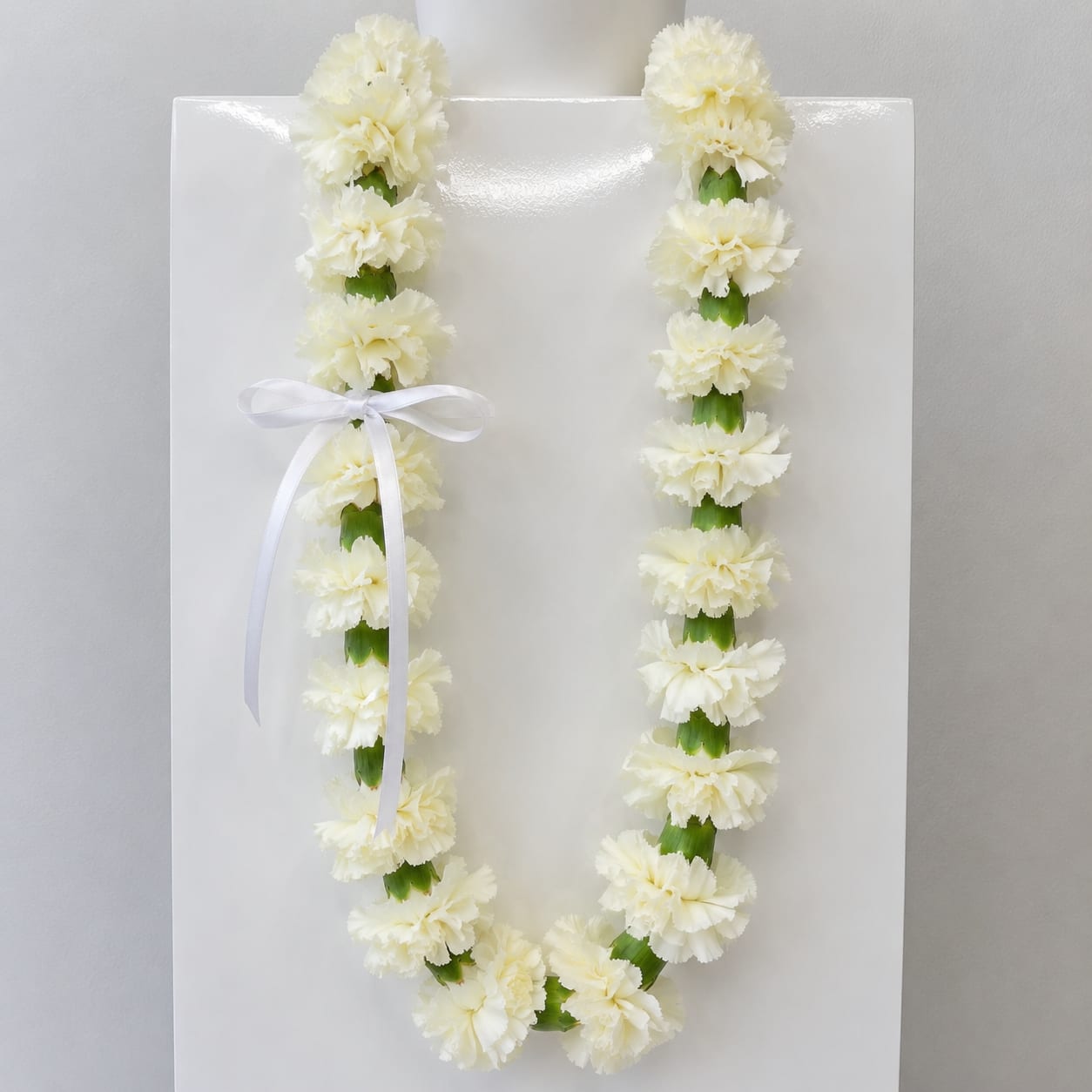 Carnation Lei - Celebrate your graduate with a classic carnation graduation lei, a timeless symbol of honor, achievement, and celebration. Available in both single strand and double strand options, these leis are handcrafted in-house with fresh carnations for a full, vibrant look that stands out on graduation day.  Offered in white, light pink, light green, and red, each color carries its own meaning while creating a beautiful, eye-catching presentation for ceremonies and photos. Carnation leis are known for their durability and long-lasting freshness, making them a perfect choice for all-day wear and keepsake memories.  Each lei is carefully designed to ensure a balanced, elegant drape, whether you choose a single strand for a classic look or a double strand for a fuller, more statement-making style. Ideal for high school and college graduations, these leis add a meaningful and celebratory touch to any milestone achievement.  Looking for a custom color? Additional colors are available upon request as a special order. Please note that all custom color requests require a minimum two-week notice to ensure availability and quality.  Order your carnation graduation lei today for pickup or delivery, and celebrate your graduate with a beautiful, traditional floral piece made just for their big day.