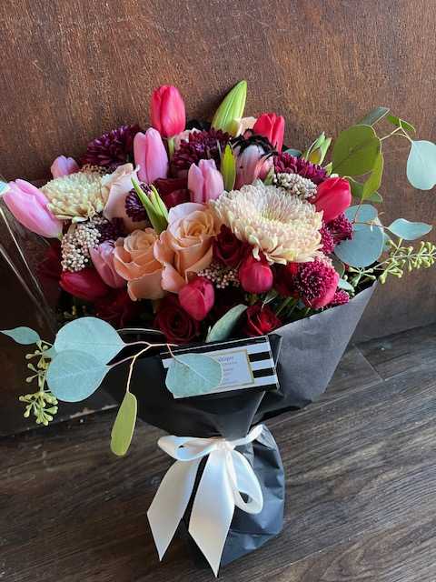 Bouquet of pink tulips, roses, and chrysanthemums wrapped in black paper