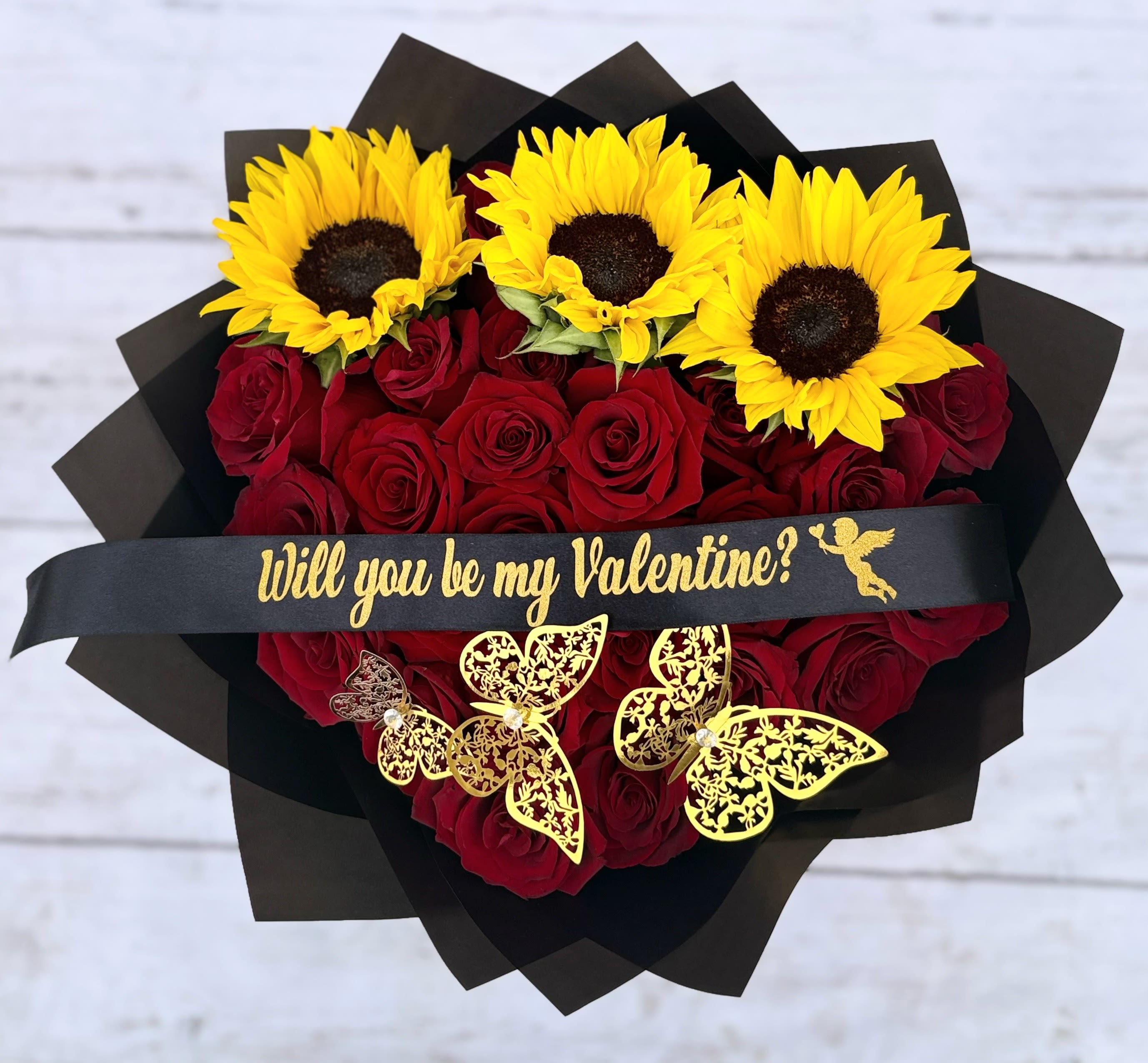 Heart-shaped bouquet of red roses topped with yellow sunflowers