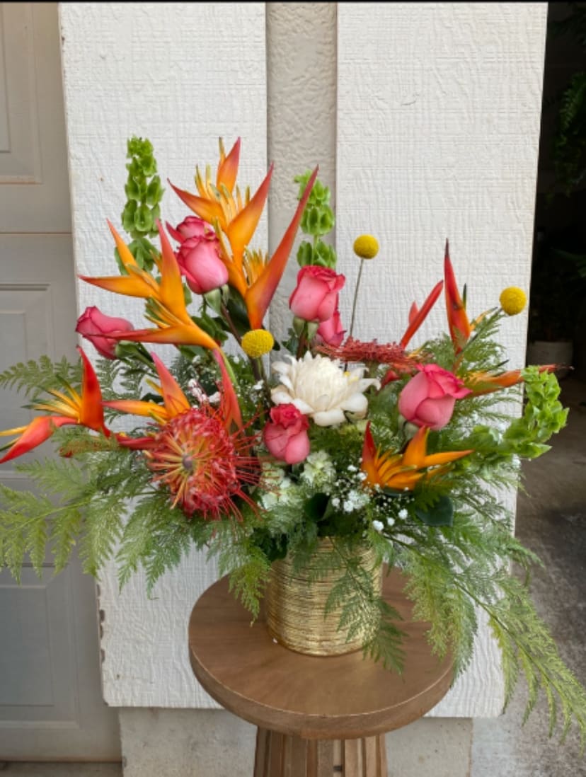 Tropical bouquet with pink roses and orange bird-of-paradise in a gold vase