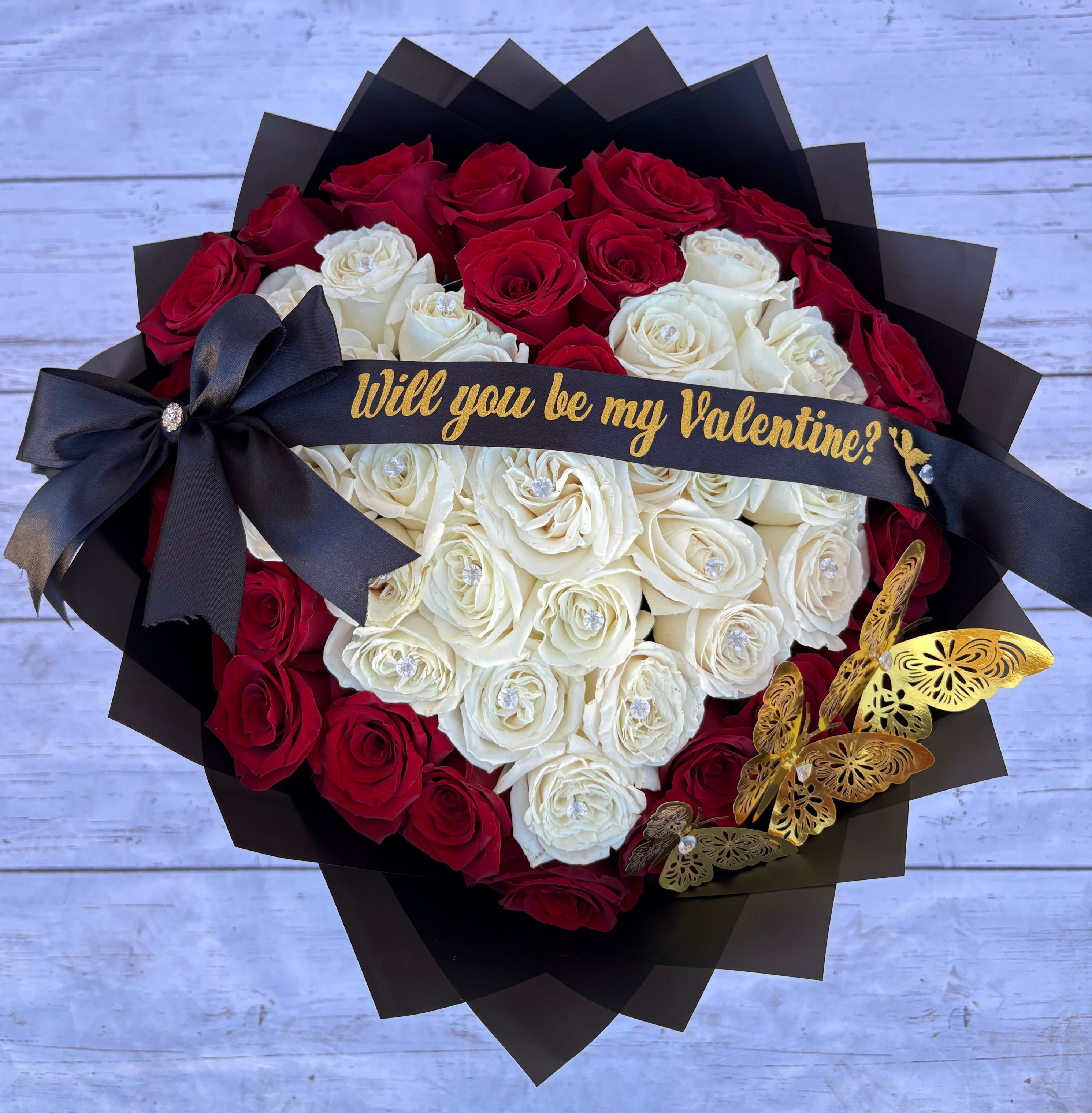 Heart-shaped bouquet of red and white roses with a black ribbon