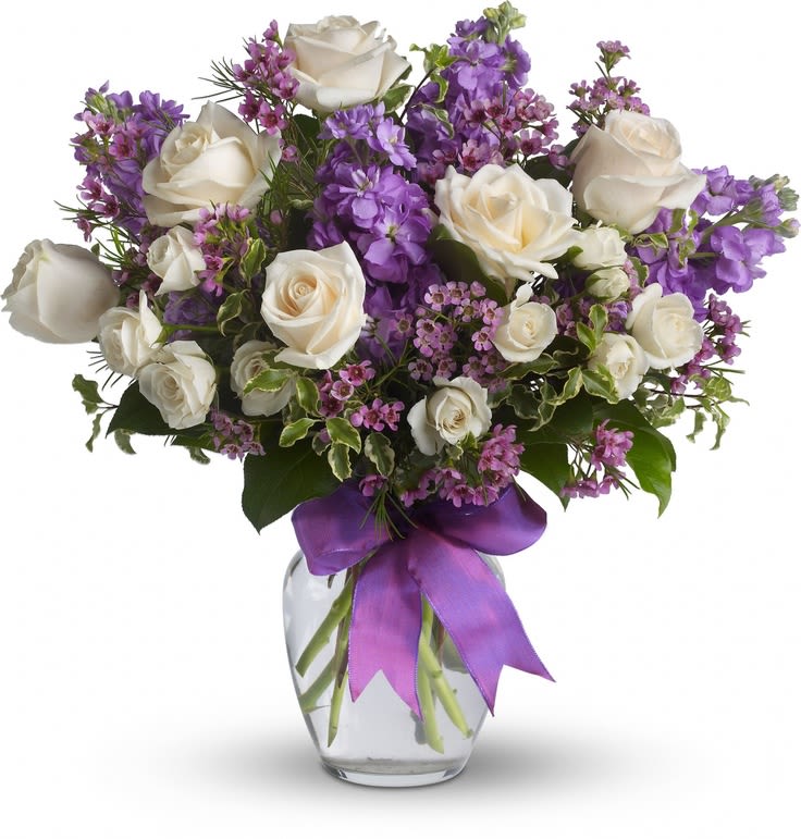 White roses and purple flowers in a glass vase with a purple ribbon