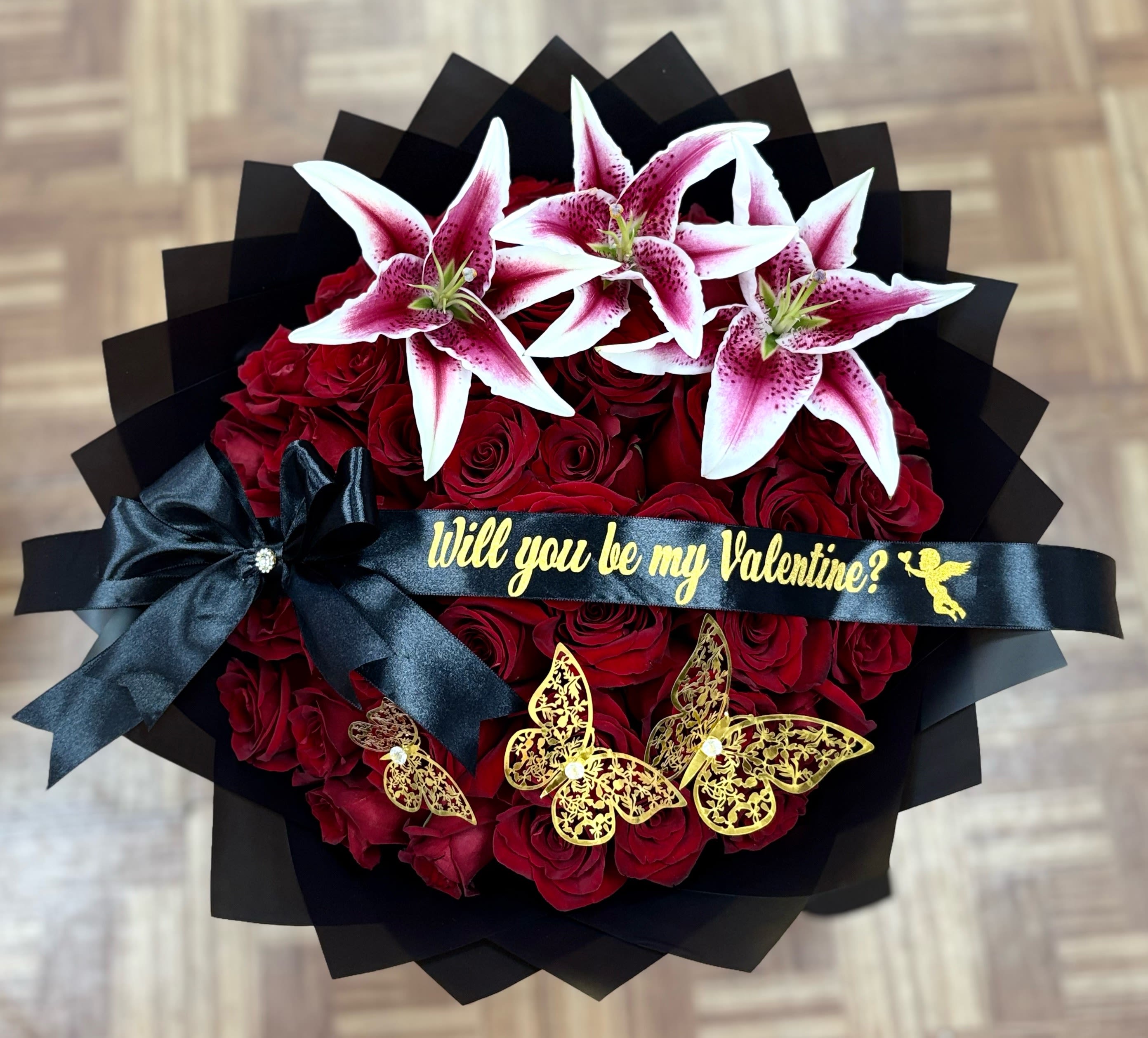 Bouquet of red roses topped with pink-and-white lilies and a black ribbon