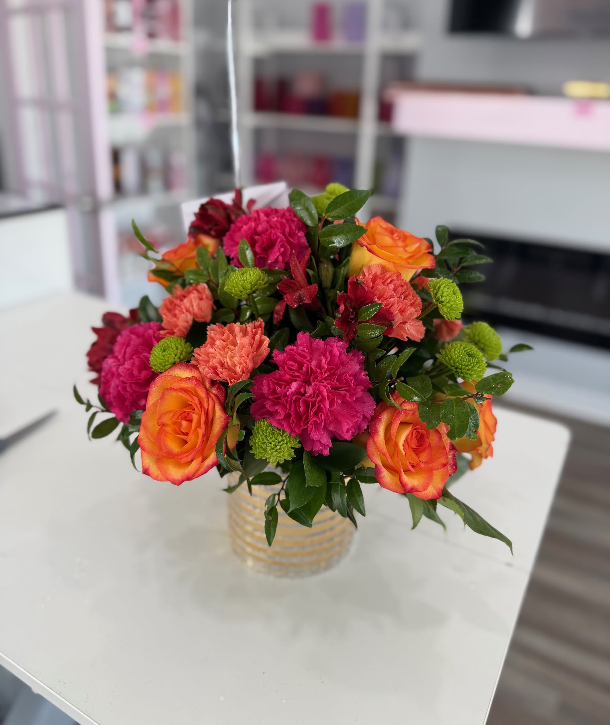 Bouquet of orange roses, pink carnations, and green button mums in a glass vase