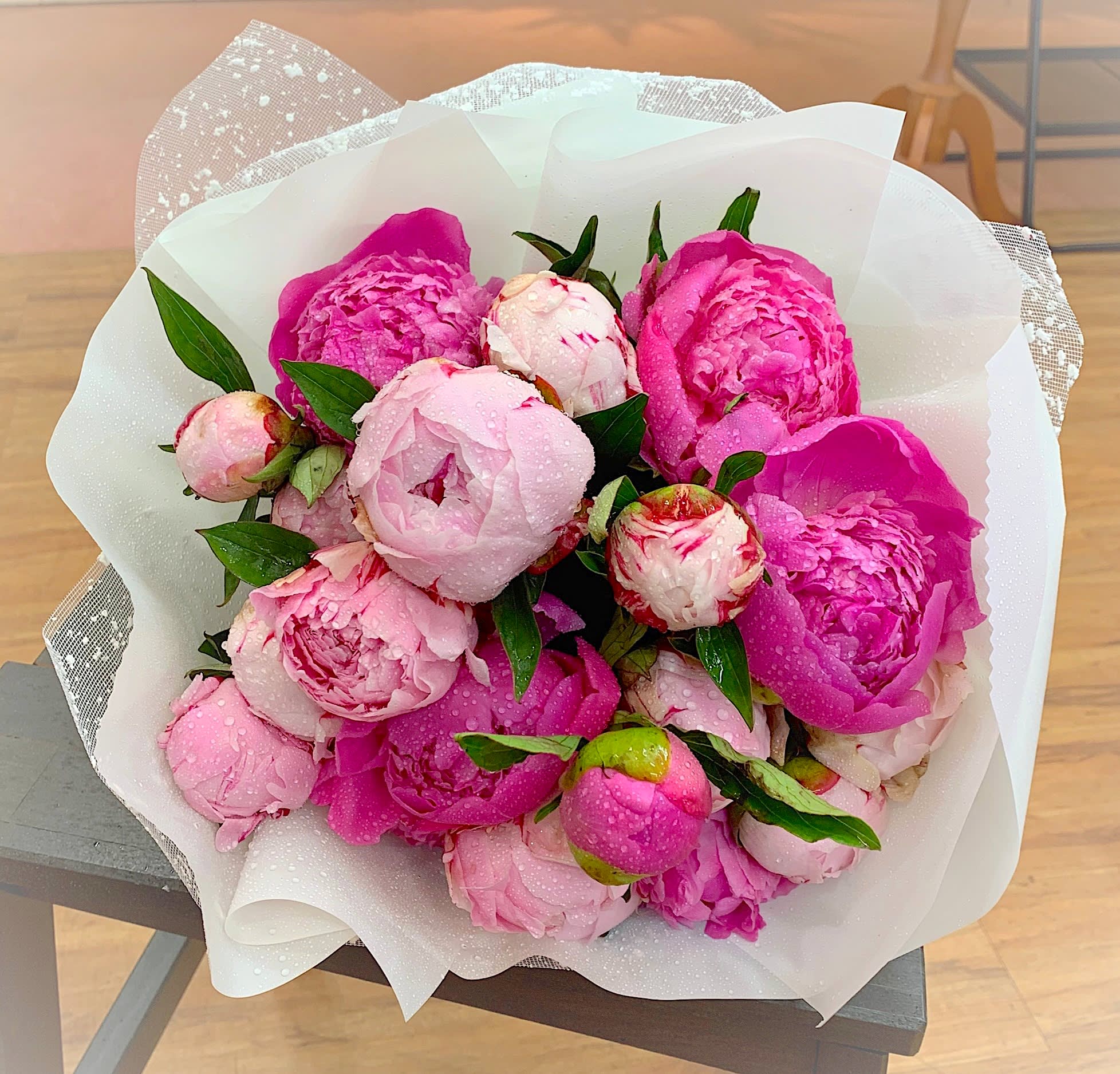 Wrapped bouquet of pink peonies with water droplets in white paper