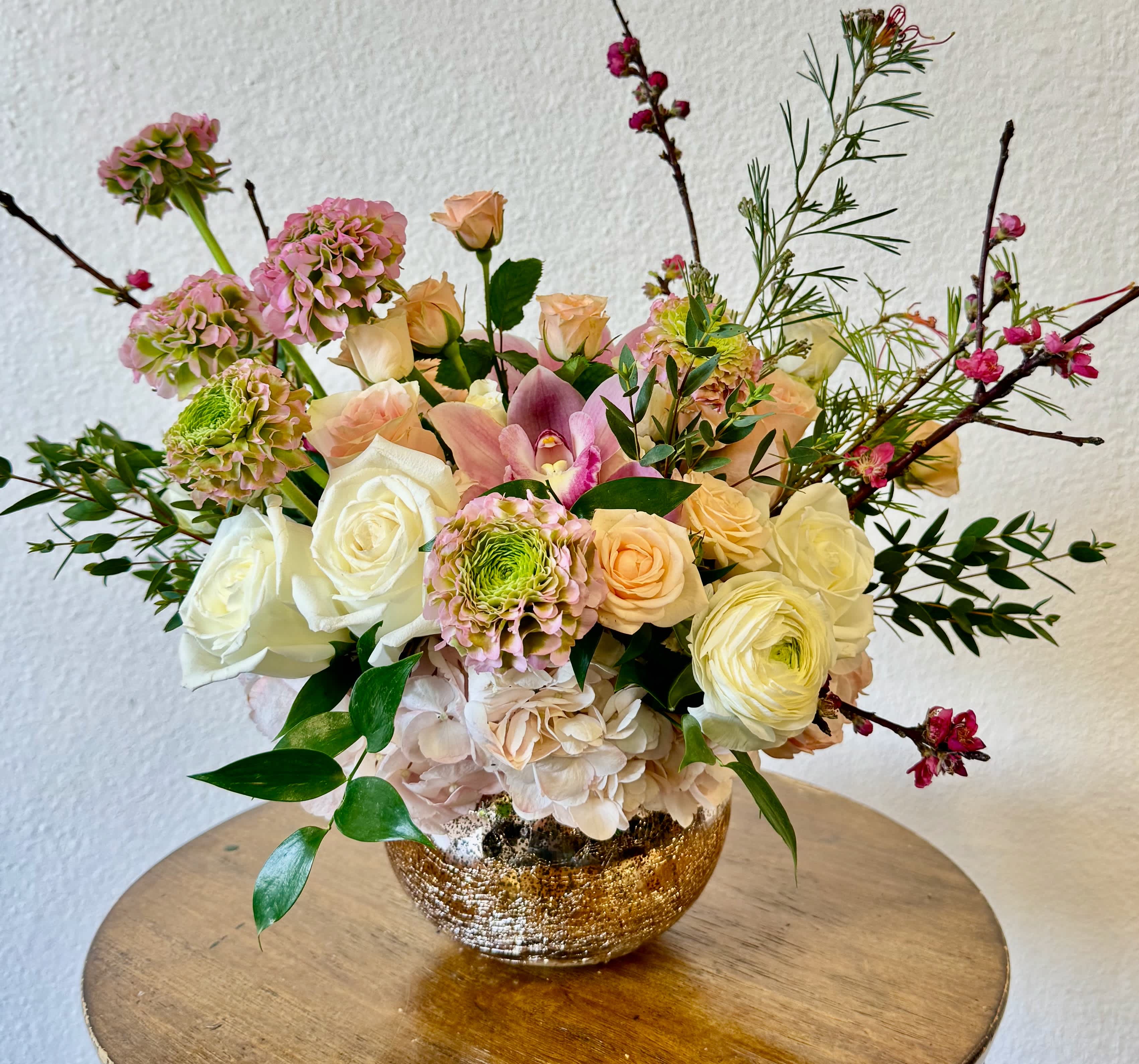 Mixed bouquet of roses, hydrangea, and orchids in a gold bowl vase