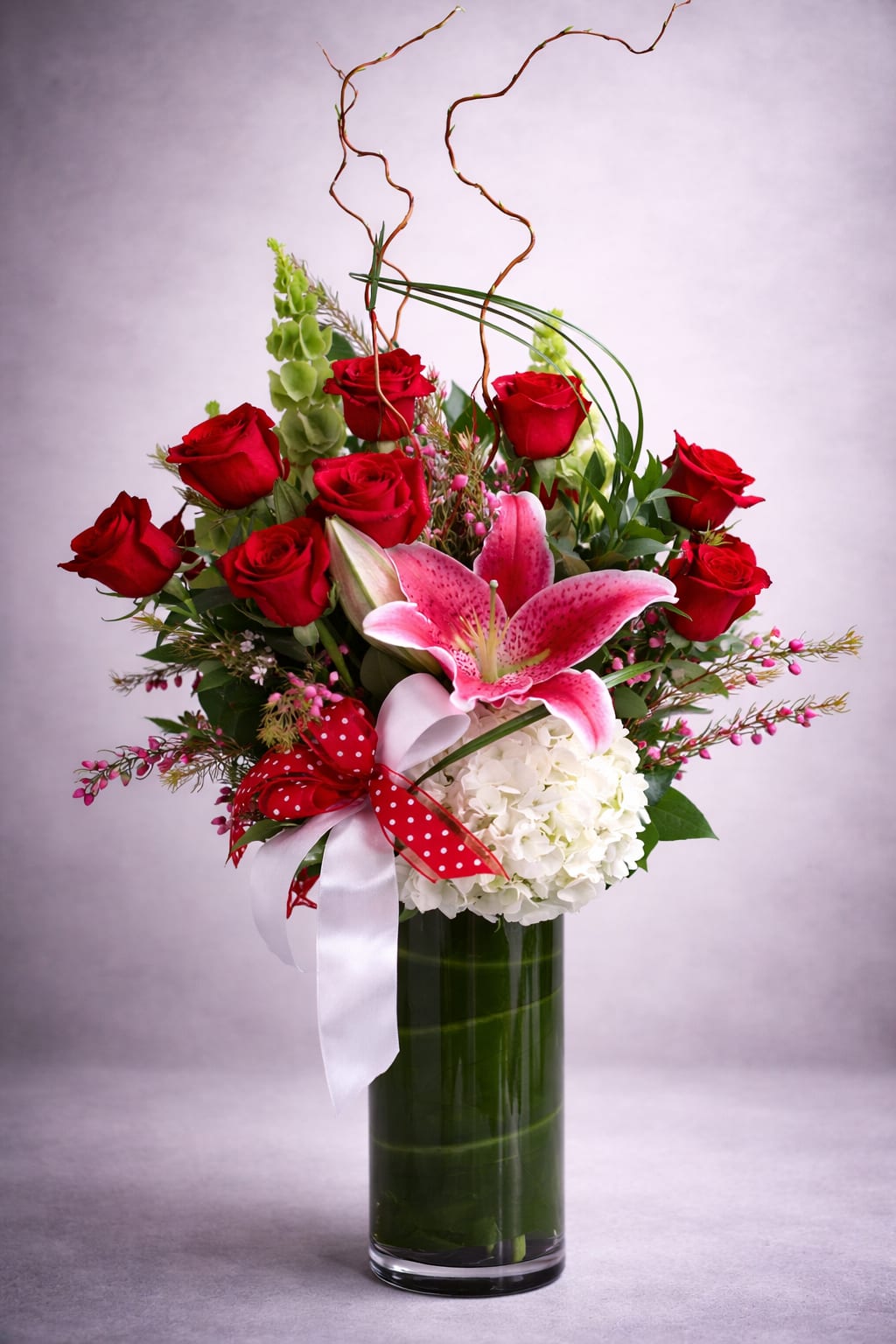 Red roses and a pink lily in a tall glass vase with ribbon