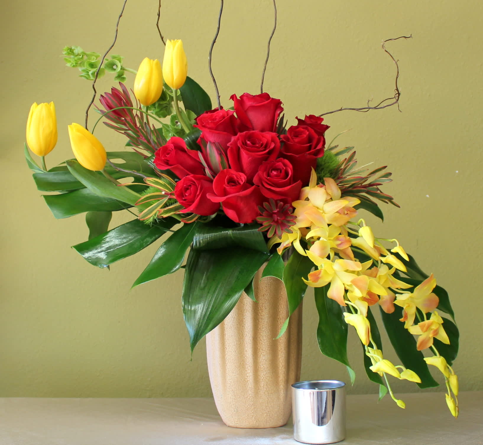 over hills for you  - Curly willow, yellow tulips red roses bells of Ireland and orchids hanging in a tall ceramic vase 