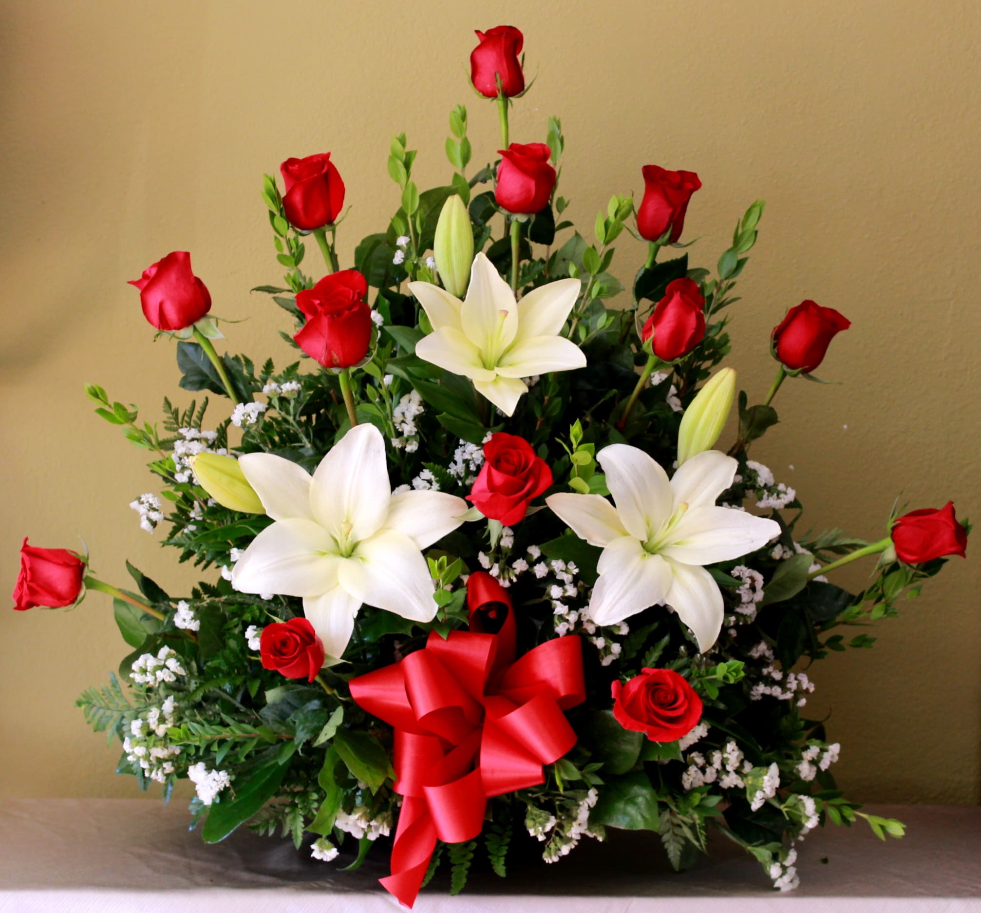 Red roses and white lilies in a low arrangement with a red ribbon bow