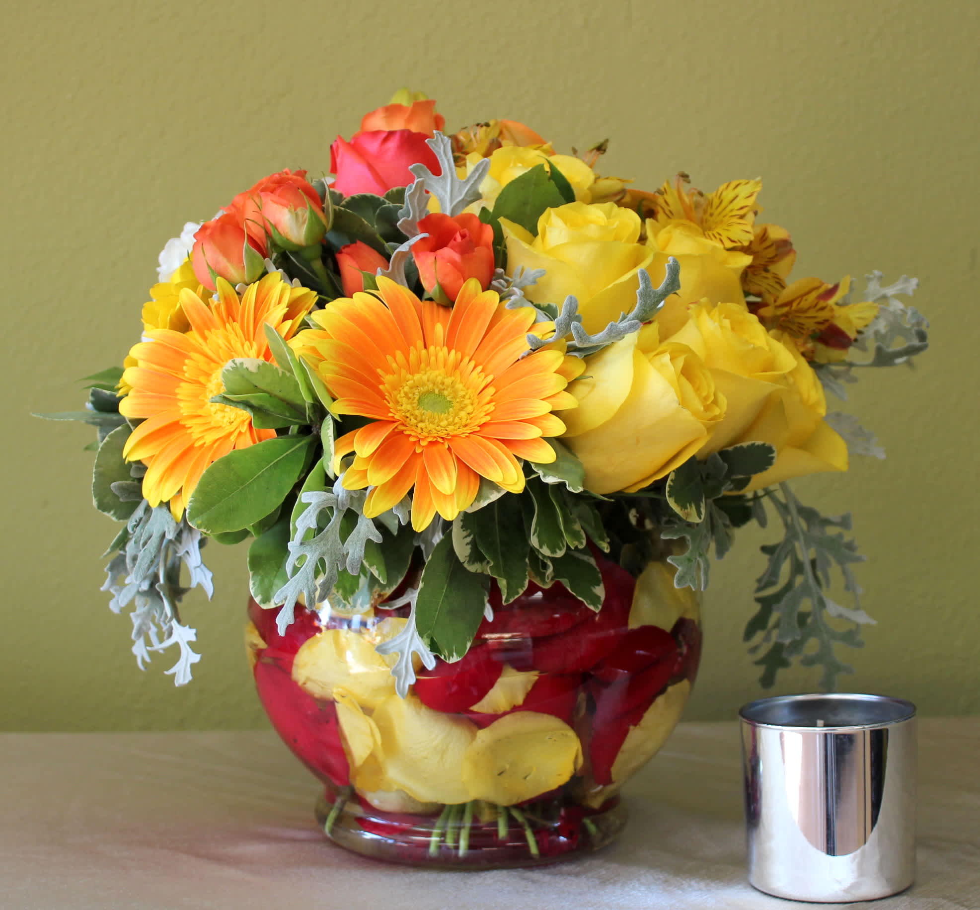 Sweet Sunshine - Orange Gerbera daisy, orange roses, yellow astromerias, dusty miller and yellow roses in a glass bubble bowl with red and yellow petals inside