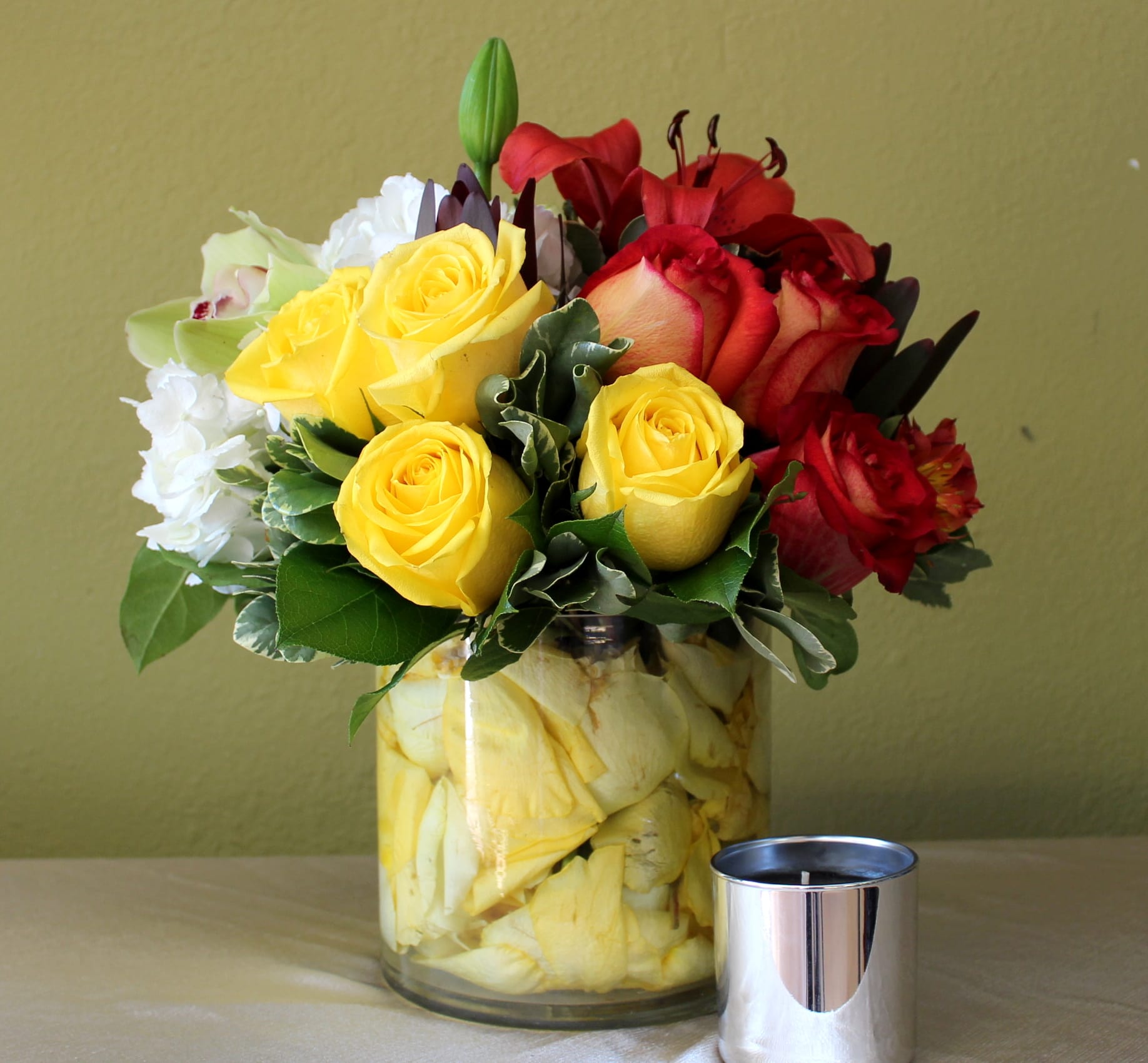 Glory of Love - Roses yellow and orange, green orchids and white hydrangeas in a clear glass cylinder with yellow petals inside  