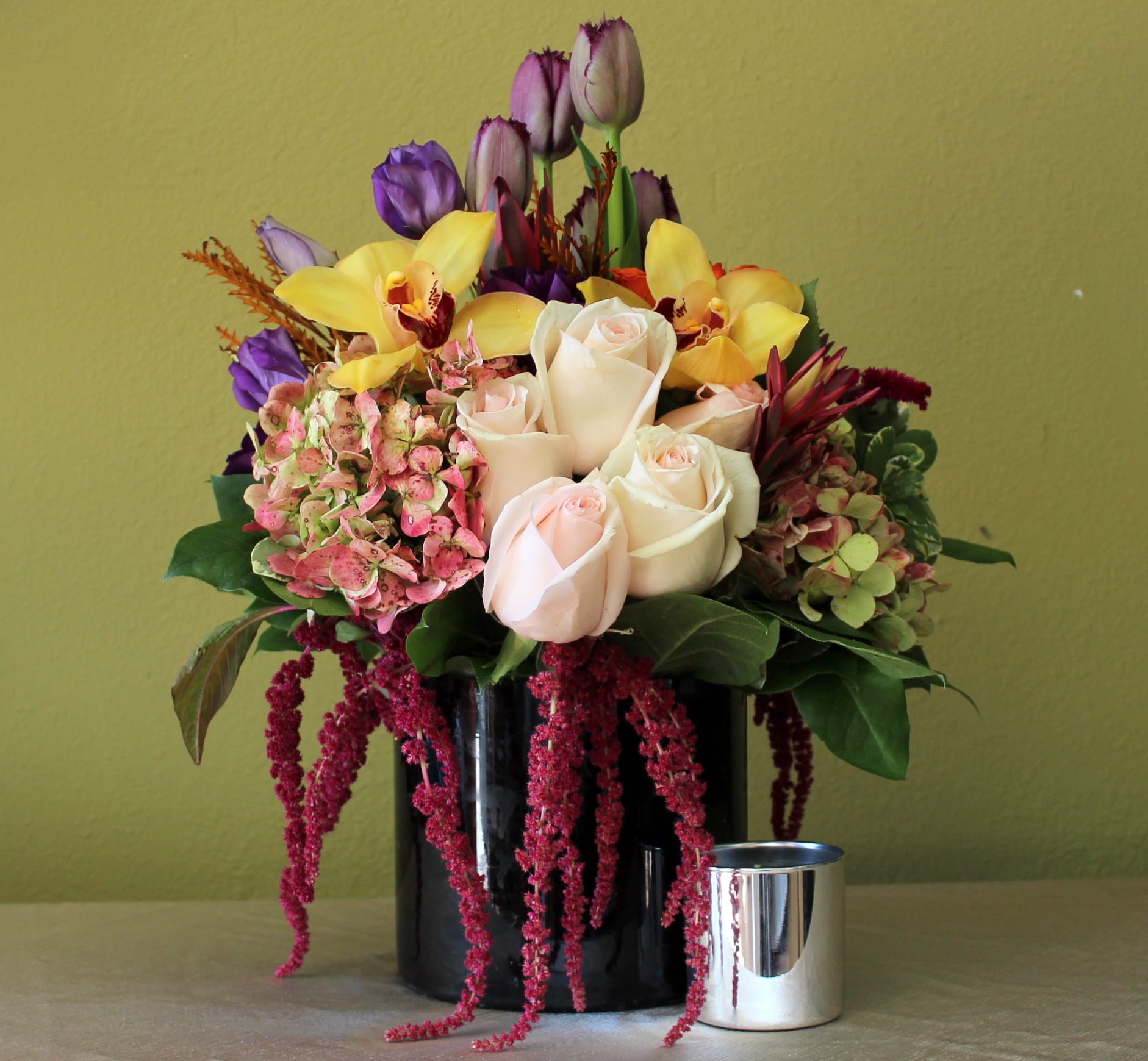 love and desire bouquet  - purple tulips, light pink long stem roses, green hydrangeas, purple  lisianthus and yellow orchids in a tall black glass cylinder 