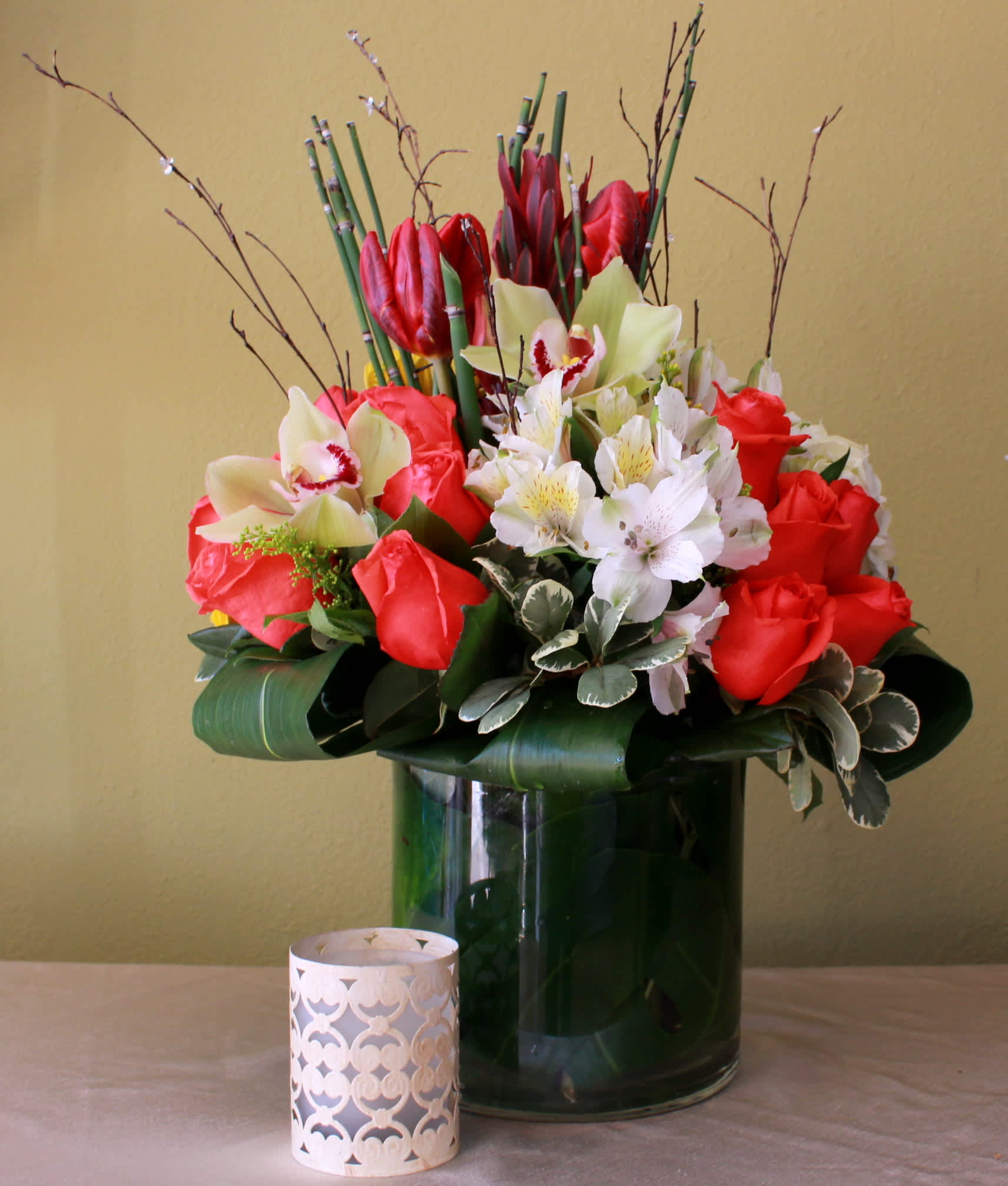 extraordinary wish  - Tall glass cylinder vase with red tulips,white astromerias hot orange roses, curly branches and cymbidium green orchids and aspidristra leaves around it. 