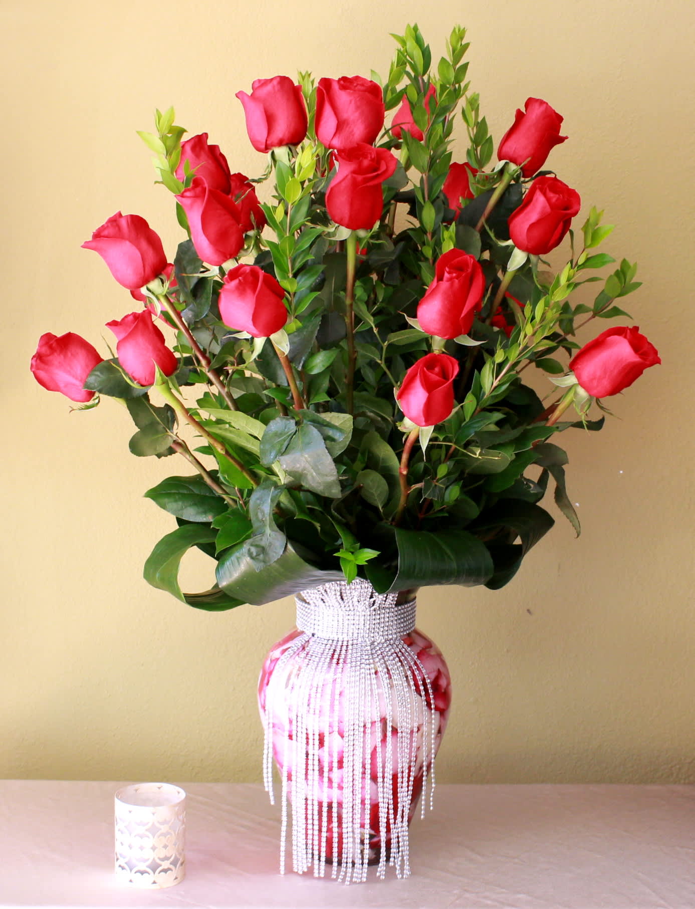 fancy lady - 24 long stem roses in a tall ginger vase dress with crystals around aspidistras leaves and other greens  