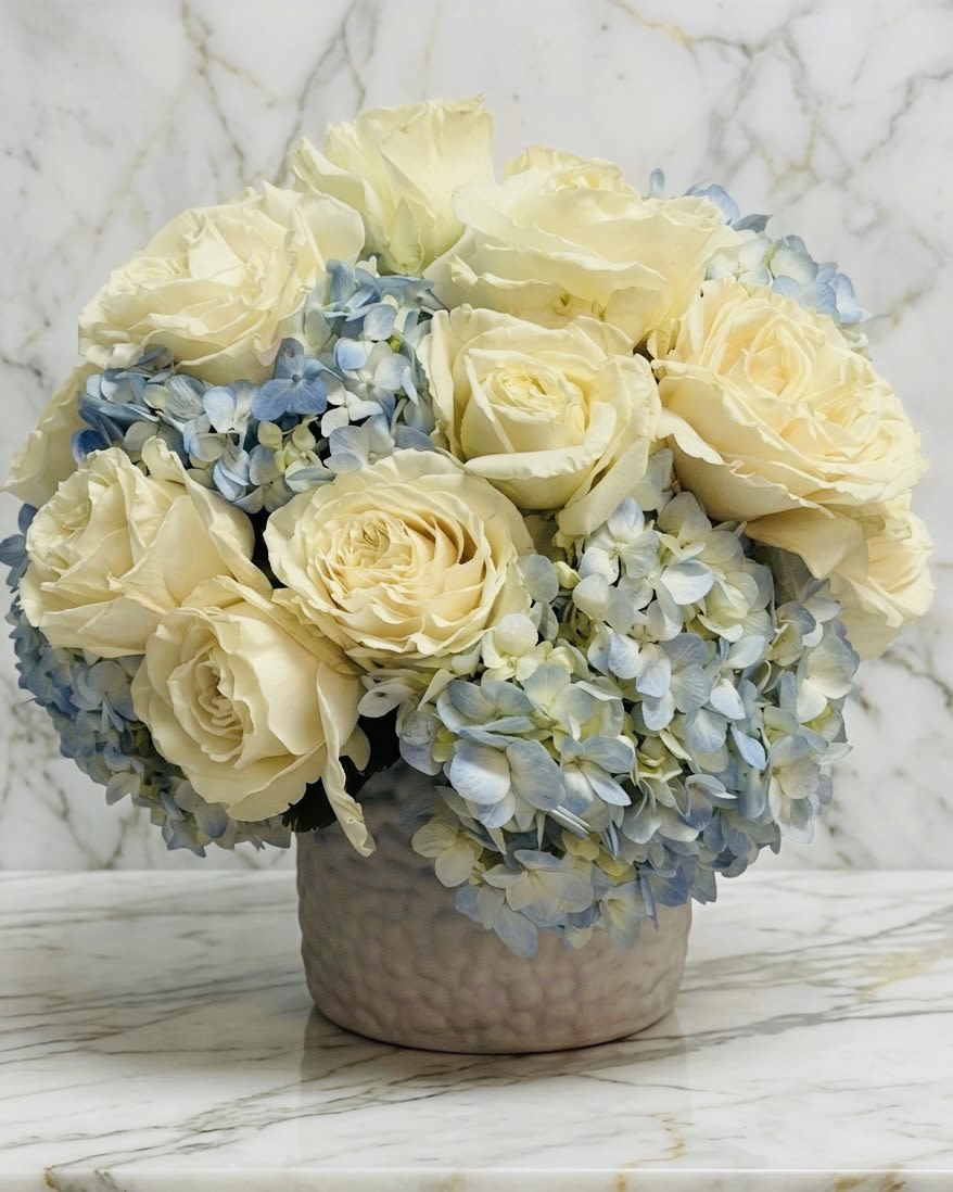 Low arrangement of ivory roses and pale blue hydrangeas in a round ceramic vase
