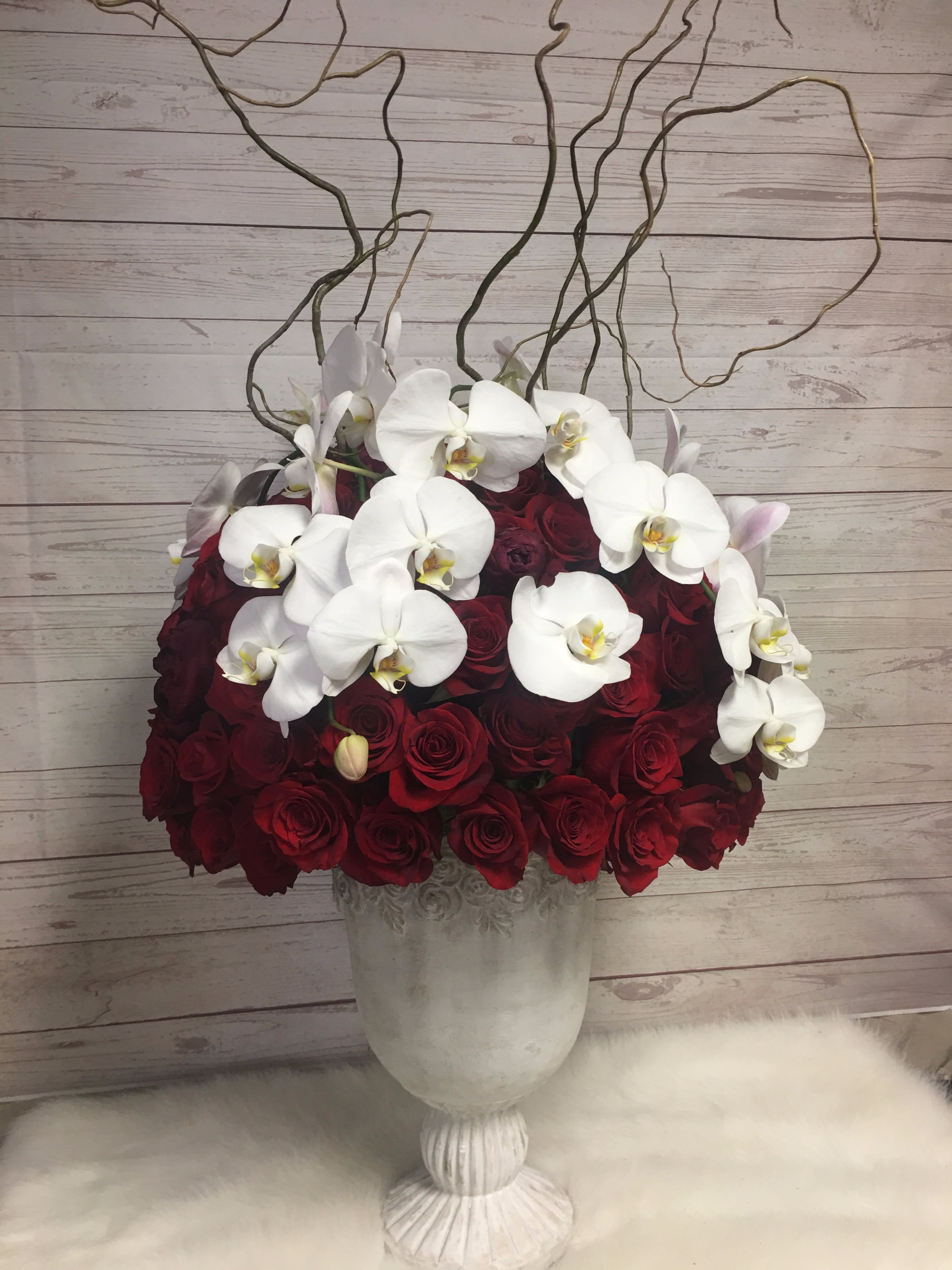 Red Rose extravagance - Romantic and extravagant red roses and white orchids arranged in a unique tall container with curly willow branches on top. 