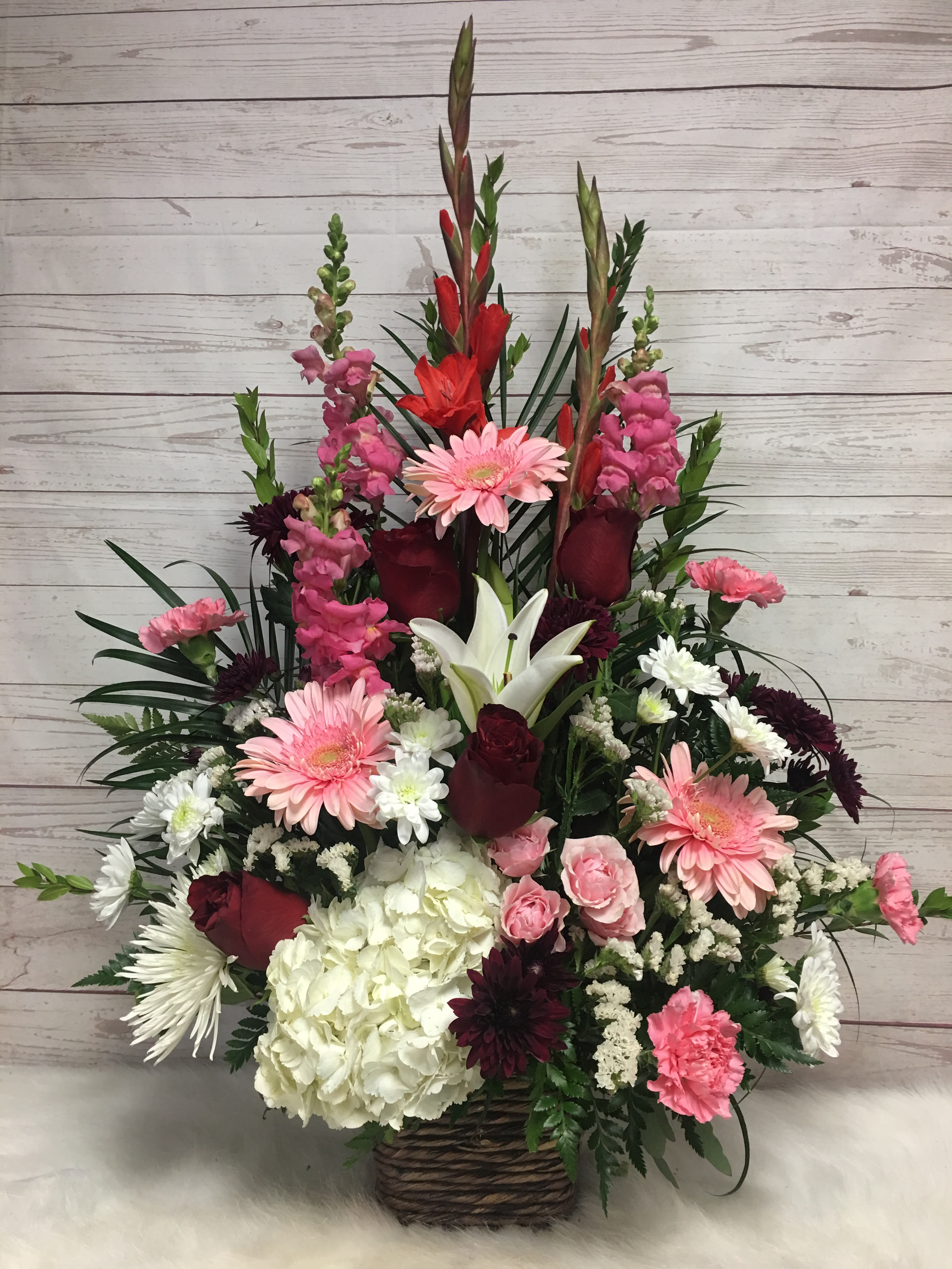 The Flower of Love - Beautifully arranged hydrangeas, pink Gerber daisies, red roses, red Gladiolas, white lilies, and carnations in a basket.