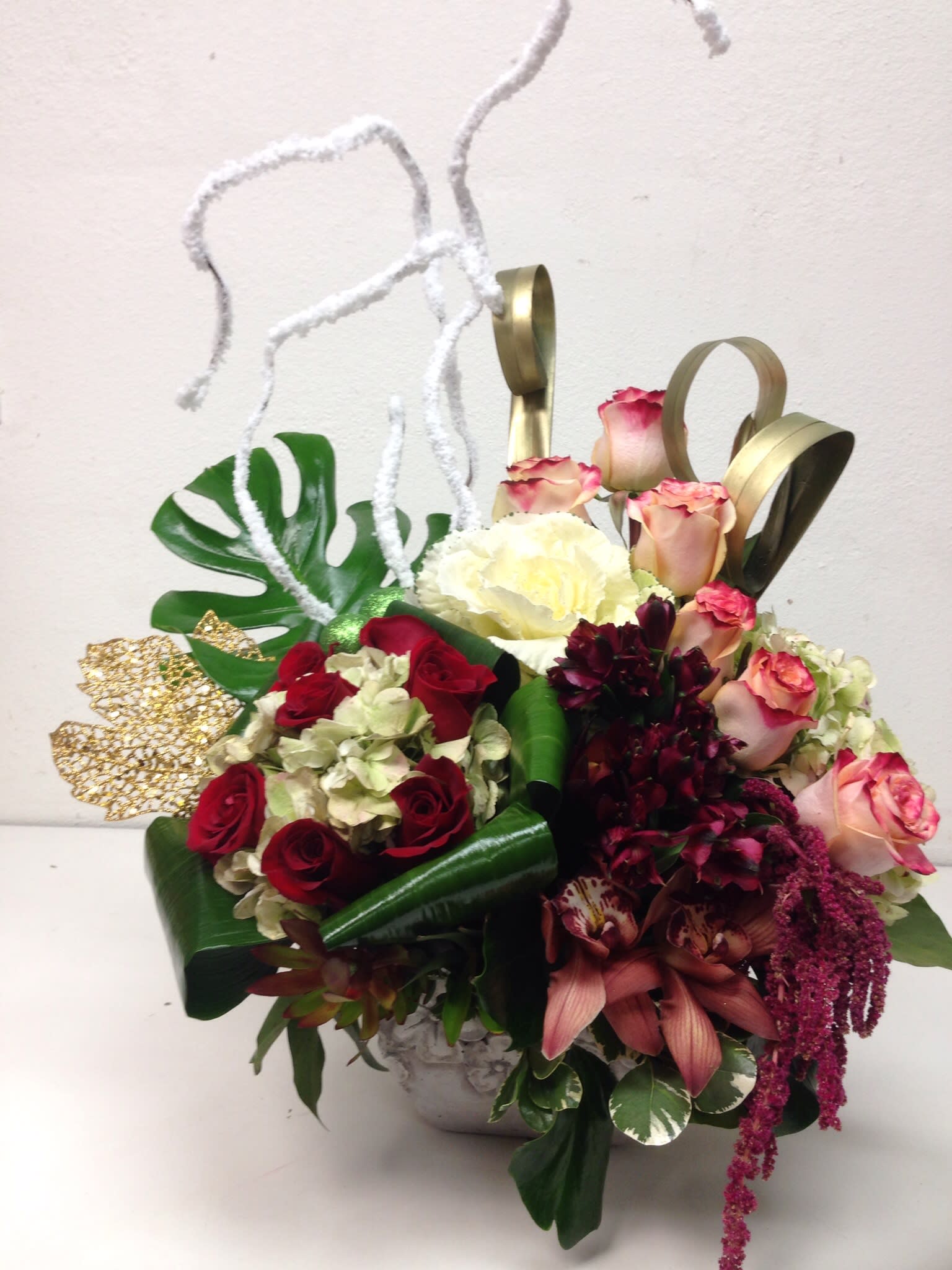 Modern  love - This artistic display features roses hydrangea, cymbidium orchids, decorative foliage, and holiday accents.