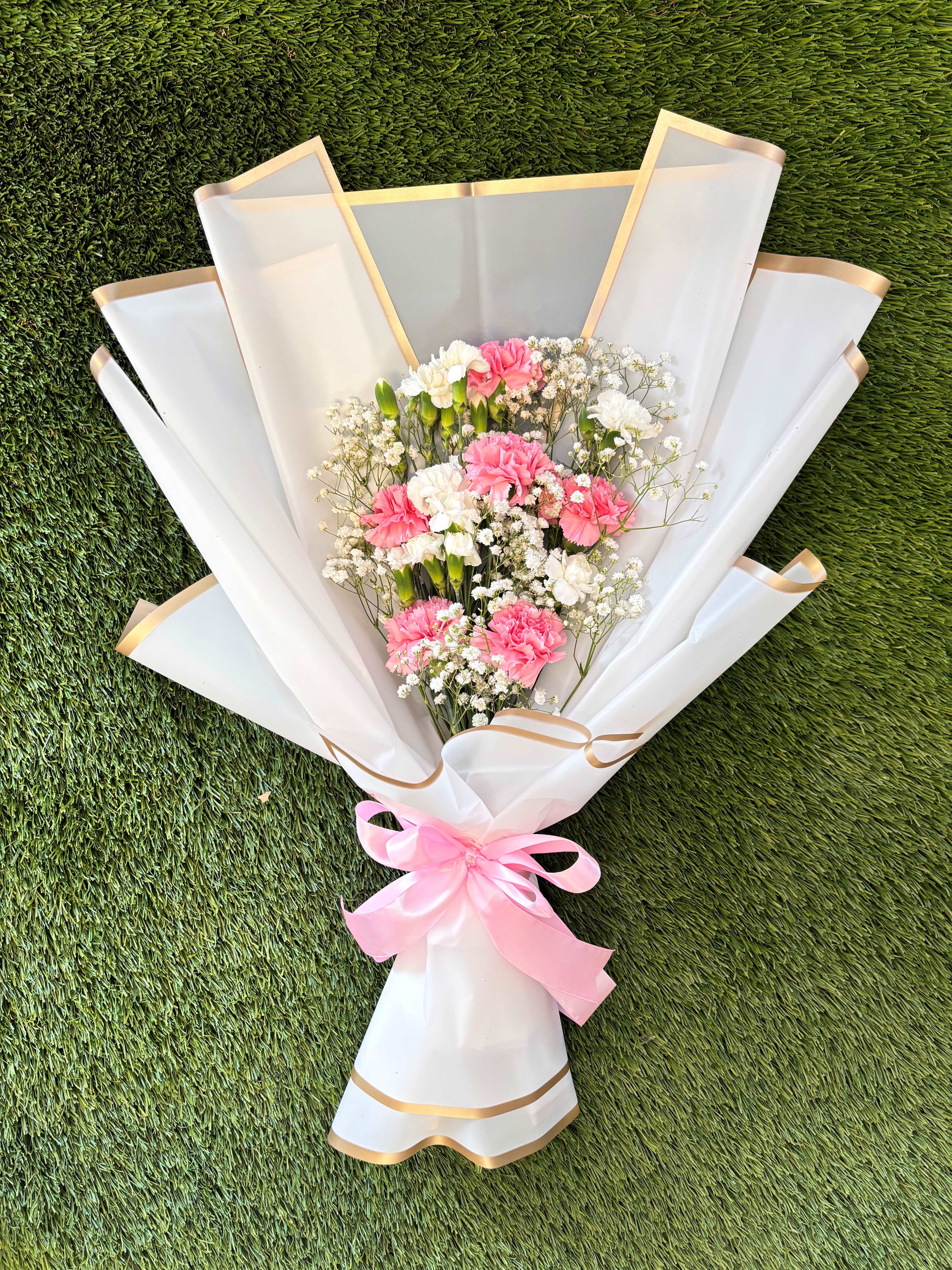 Pink and white carnation bouquet wrapped in white paper with a pink ribbon