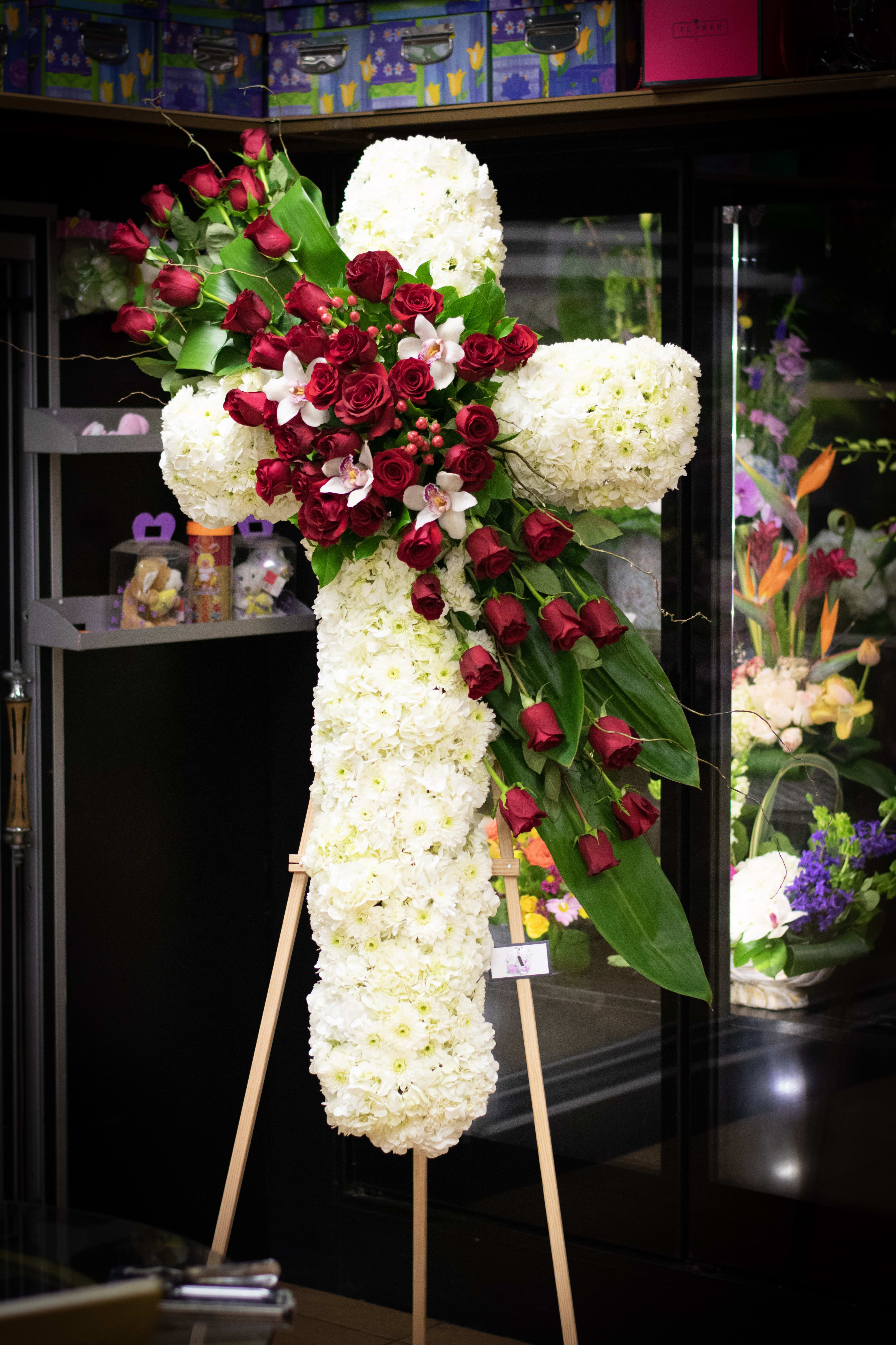 Large cross-shaped floral tribute with white blooms and red roses on an easel