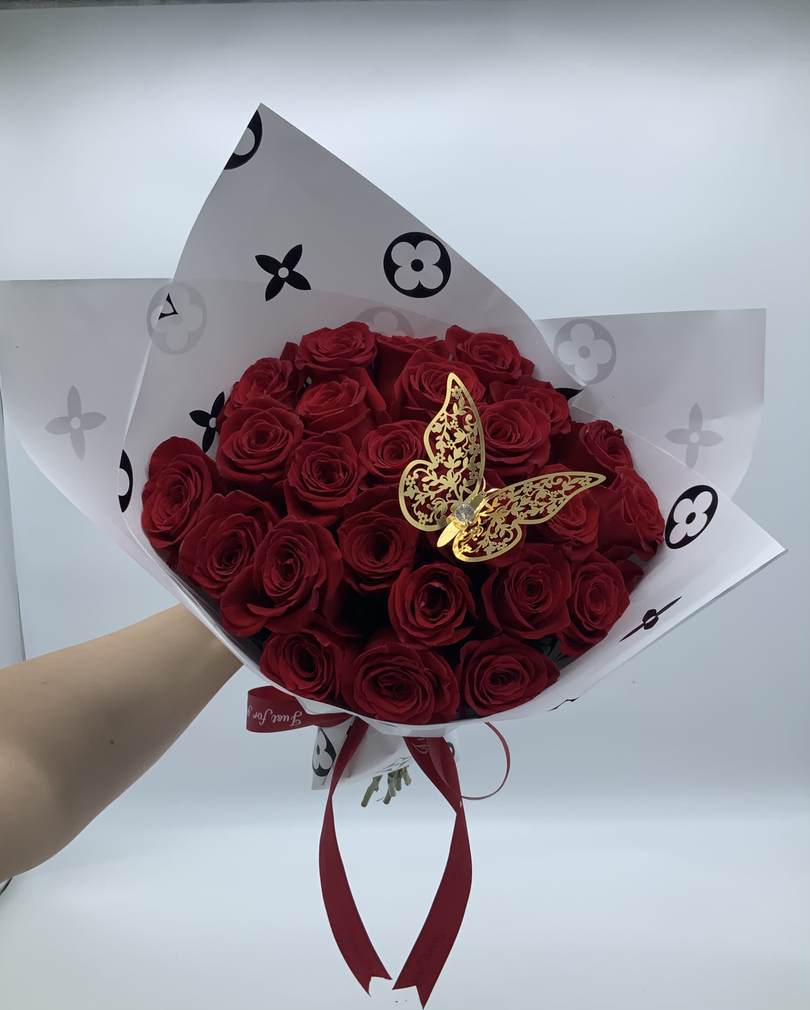 Bouquet of red roses wrapped in white paper with a gold butterfly accent