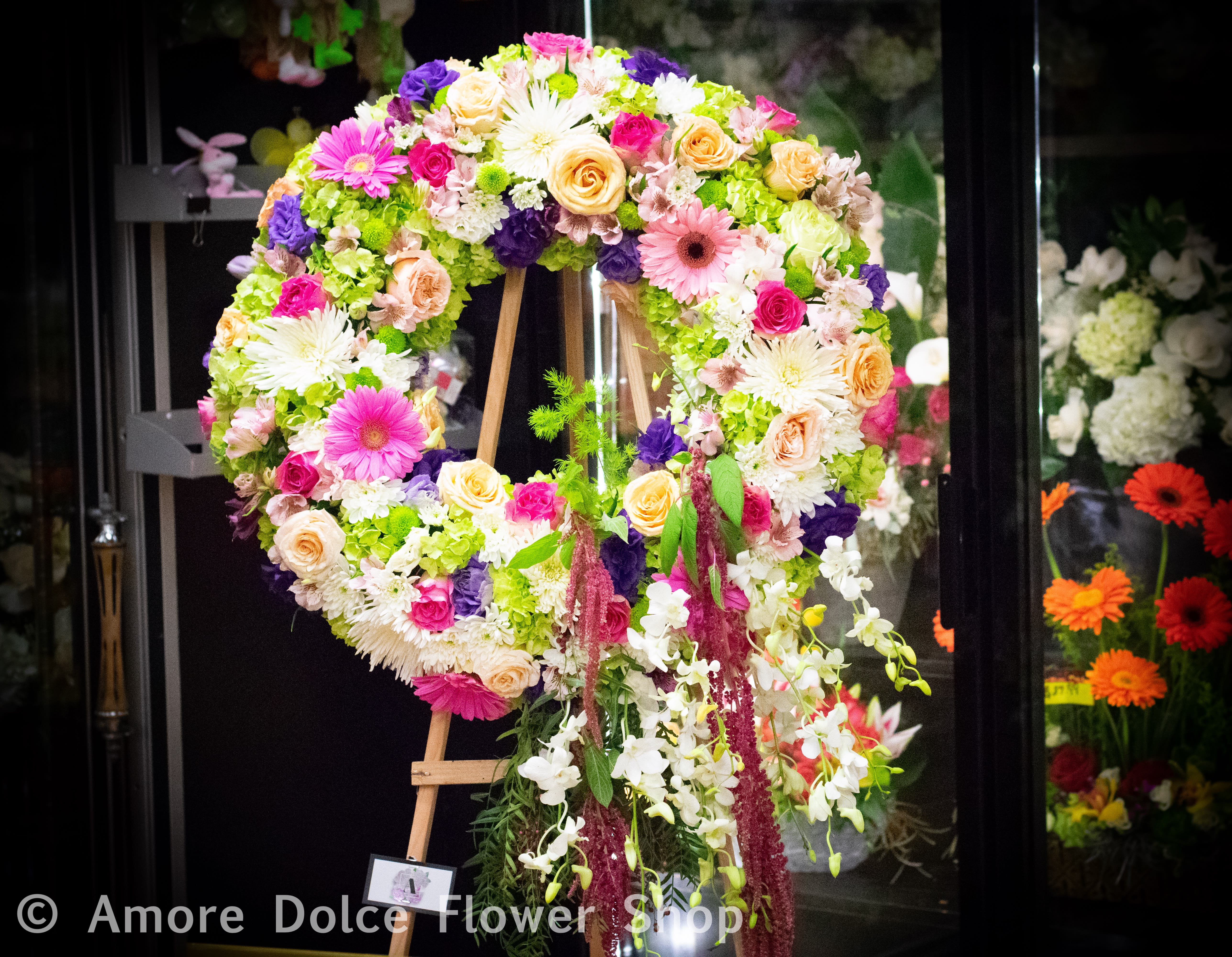 Large floral wreath on an easel with pink, white, peach, and purple flowers.