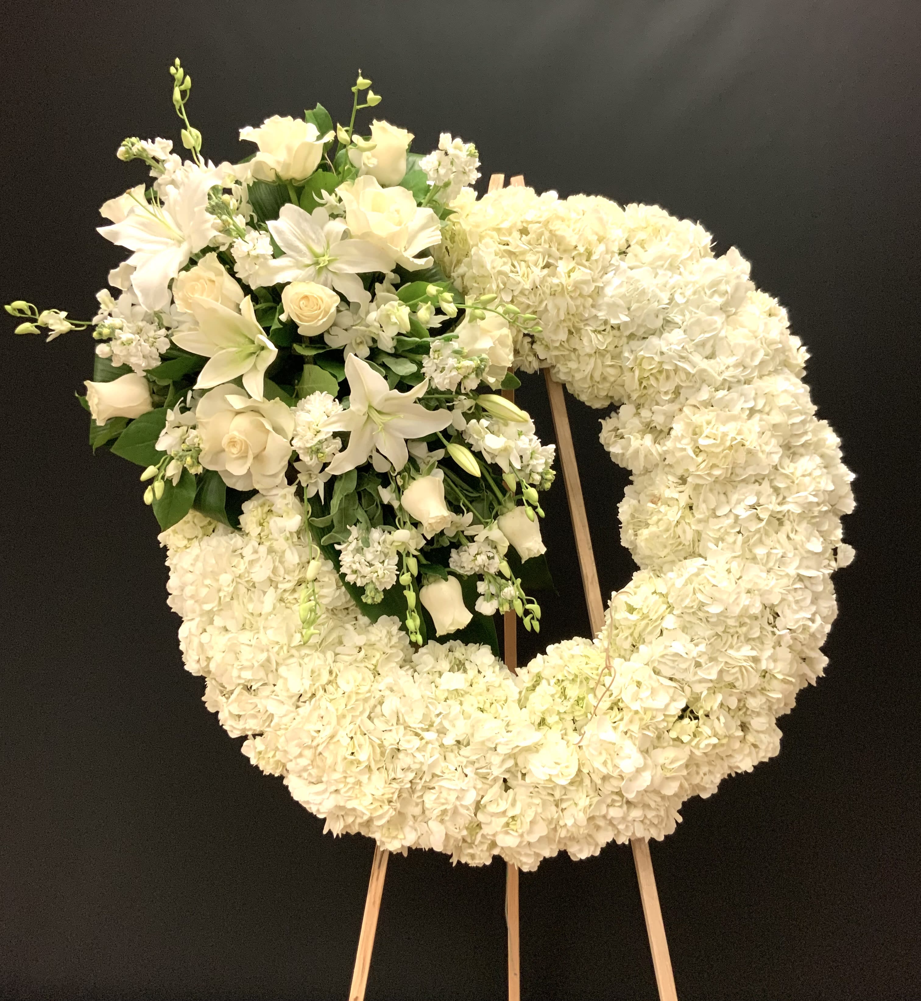 White floral wreath on an easel with a cluster of lilies and roses