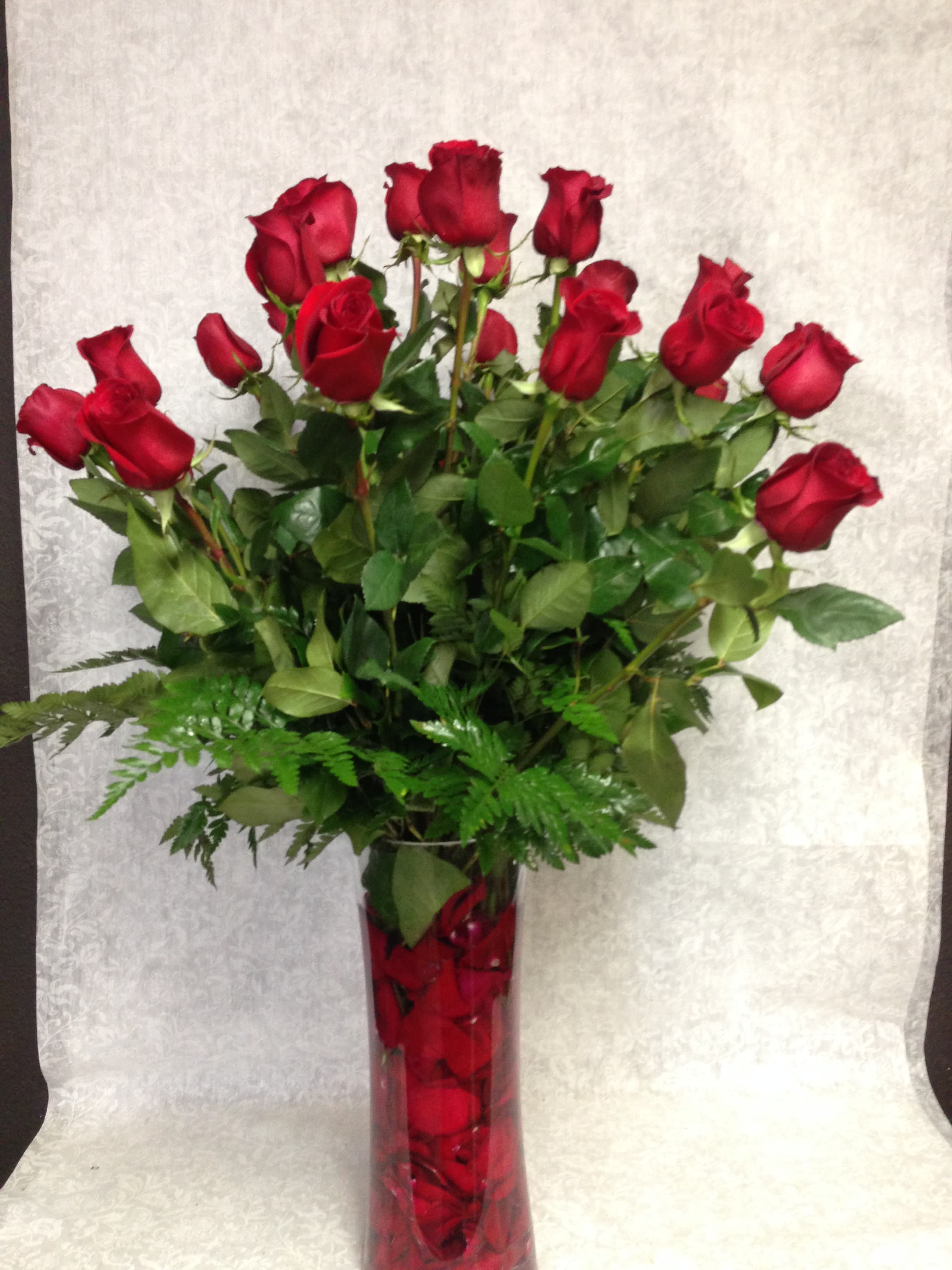 Elegant and Lovely - Two dozen long stem red roses in a tall cylinder vase with romantic red rose petals inside.