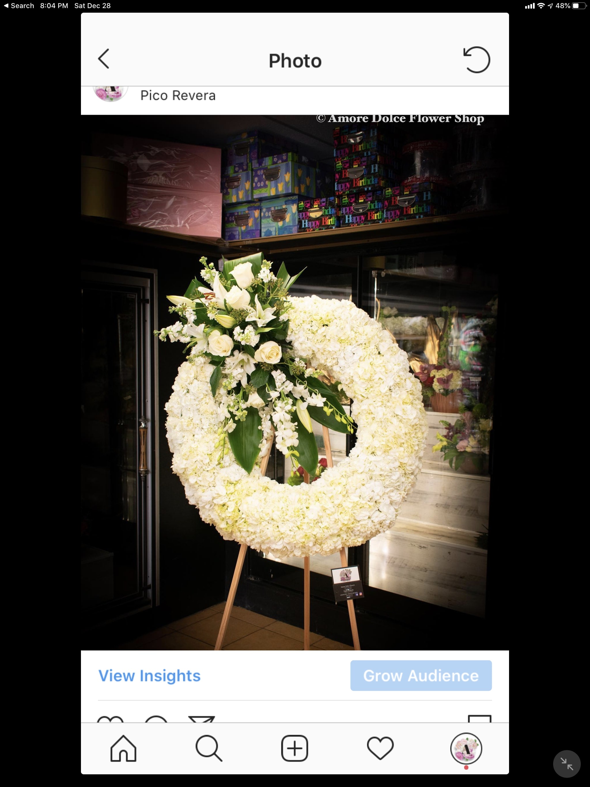 White floral funeral wreath on a wooden easel with lilies and roses