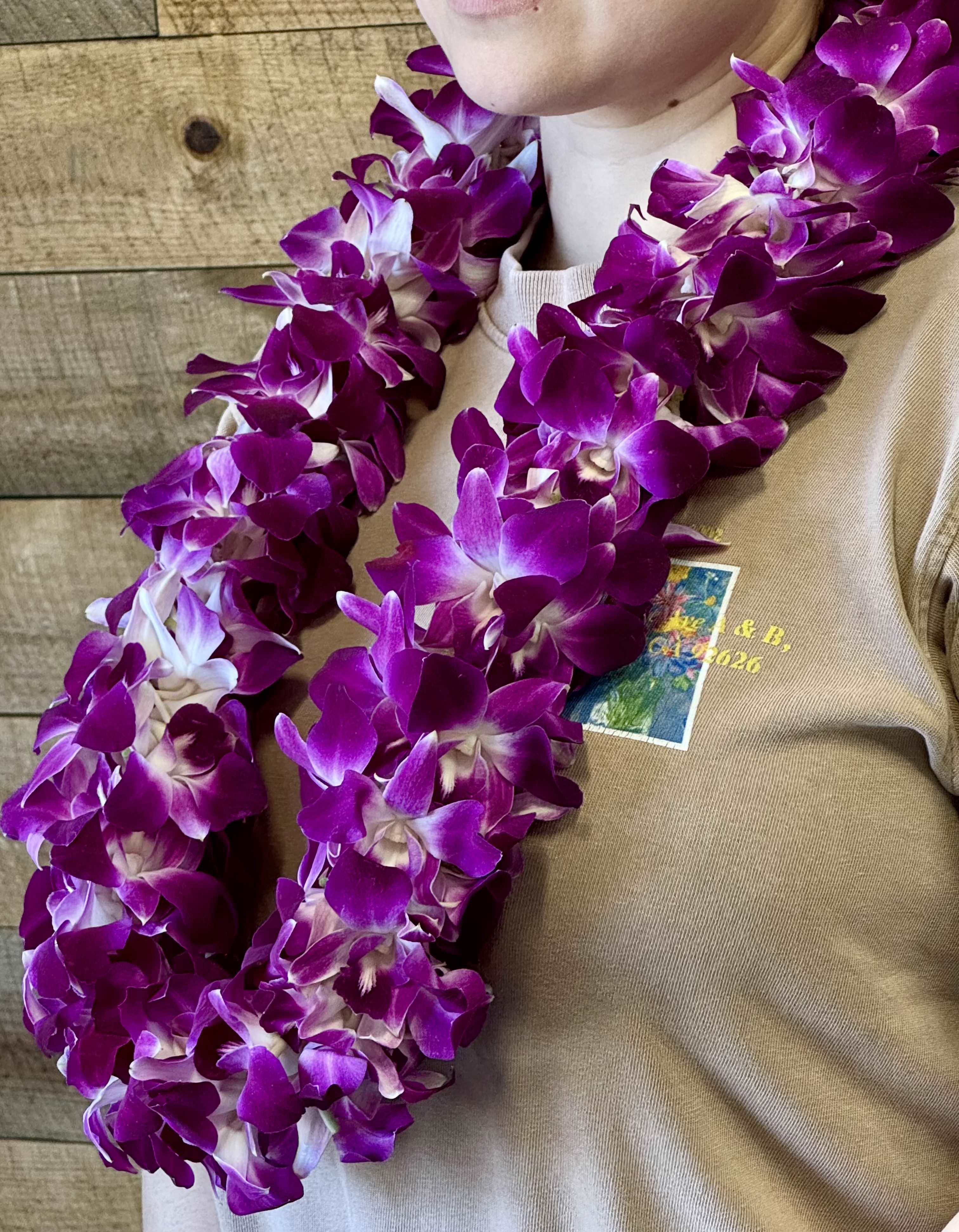 Purple orchid lei draped around a person wearing a tan shirt