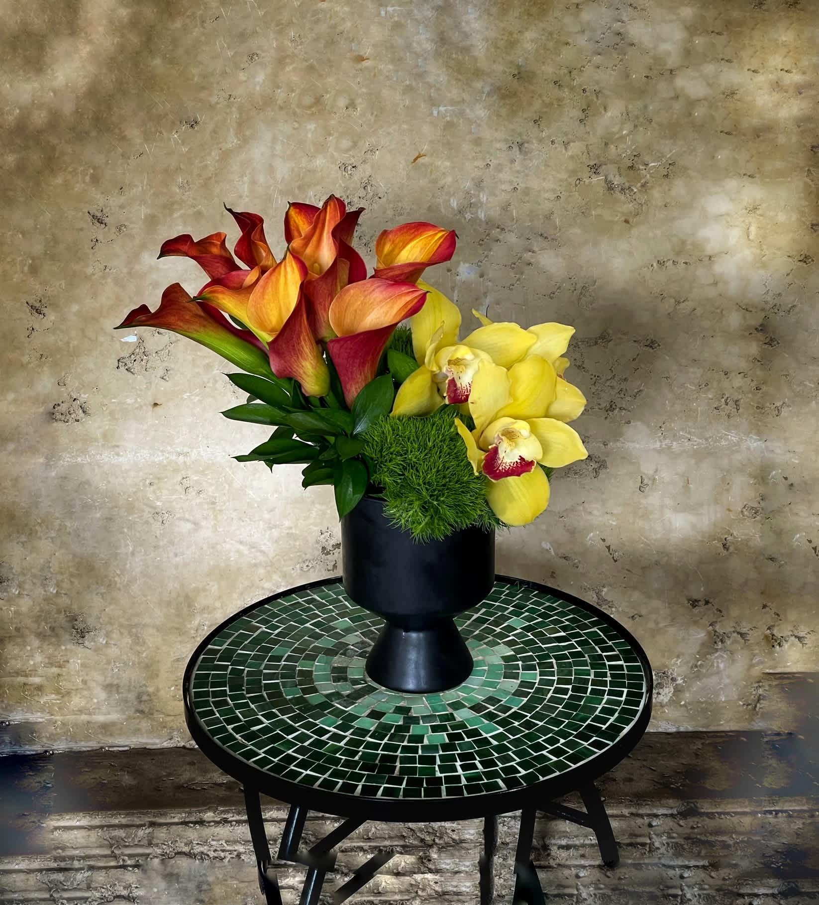 Arrangement of red-orange calla lilies and yellow orchids in a black vase