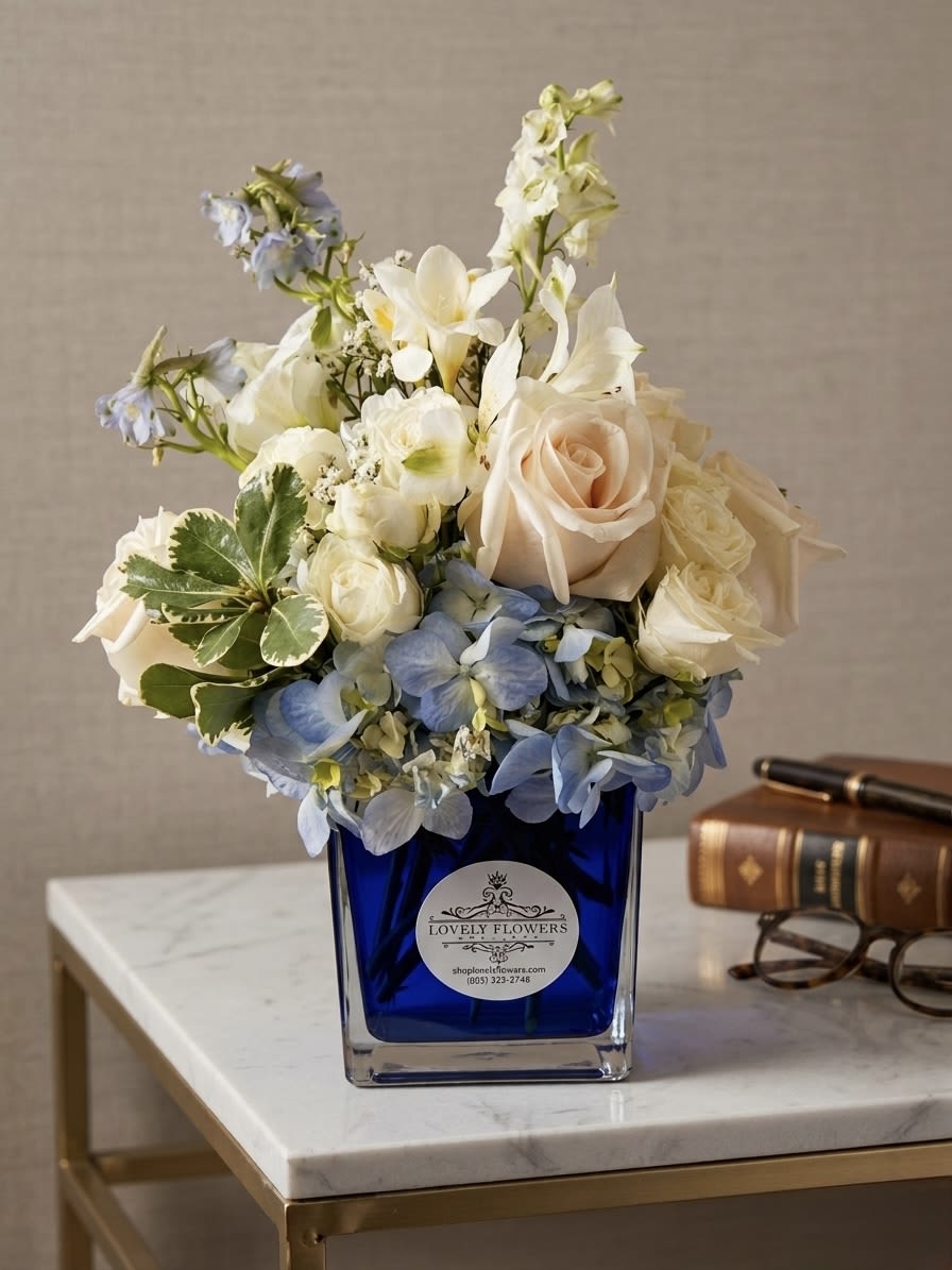 The Executive - This Father’s Day, gift a statement of strength and sophistication. The Executive pairs a bold foundation of serene blue hydrangea with premium ivory roses, creating a look of calm authority. Set in a distinguished cobalt glass vase, this architectural arrangement is the perfect refined accent for his desk or home office. Elevate his space with a gift that defines understated luxury and professional class.