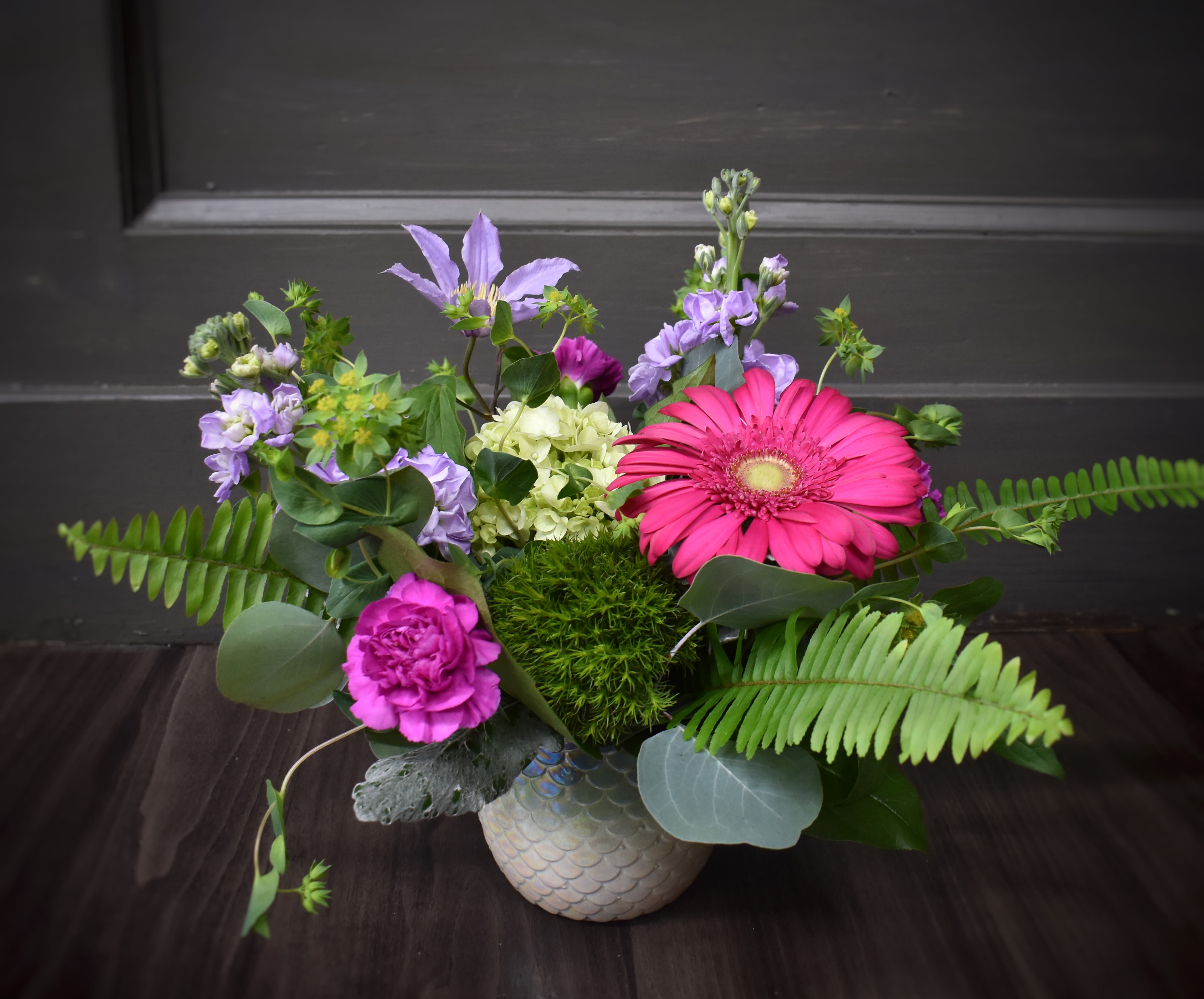 Siren's Song - A pretty ceramic container with an iridescent finish is filled with brightly colored flowers including fragrant stock, carnations, Gerber daisy and other foliages and flowers.