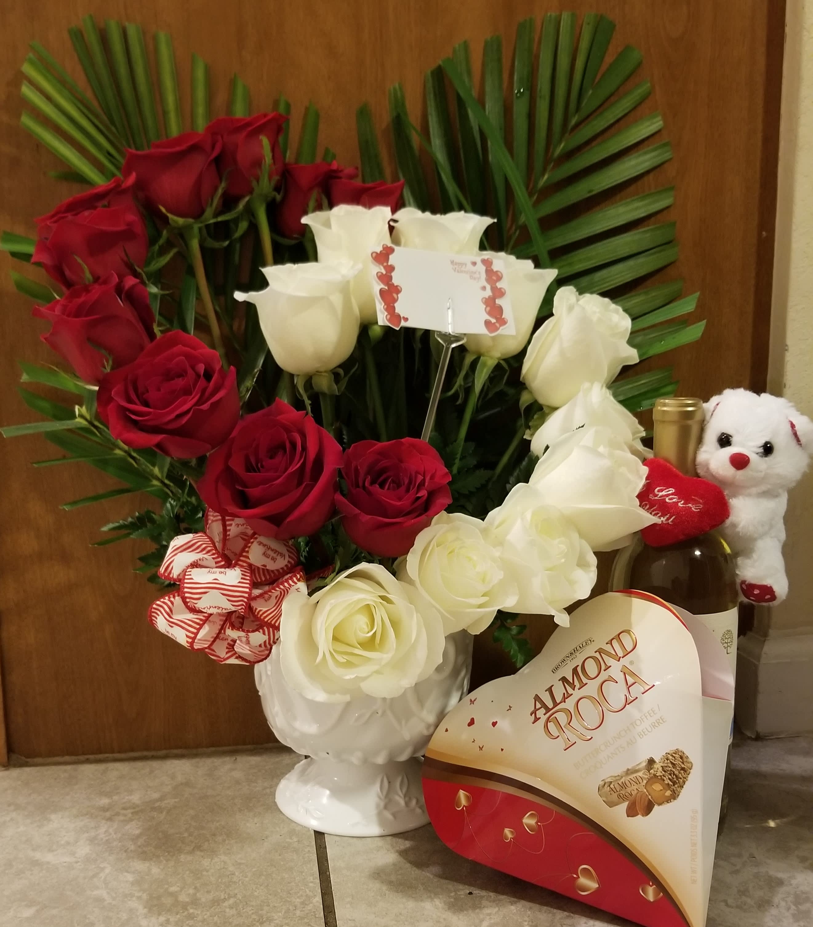 Red and white roses in a white vase with chocolates and a teddy bear