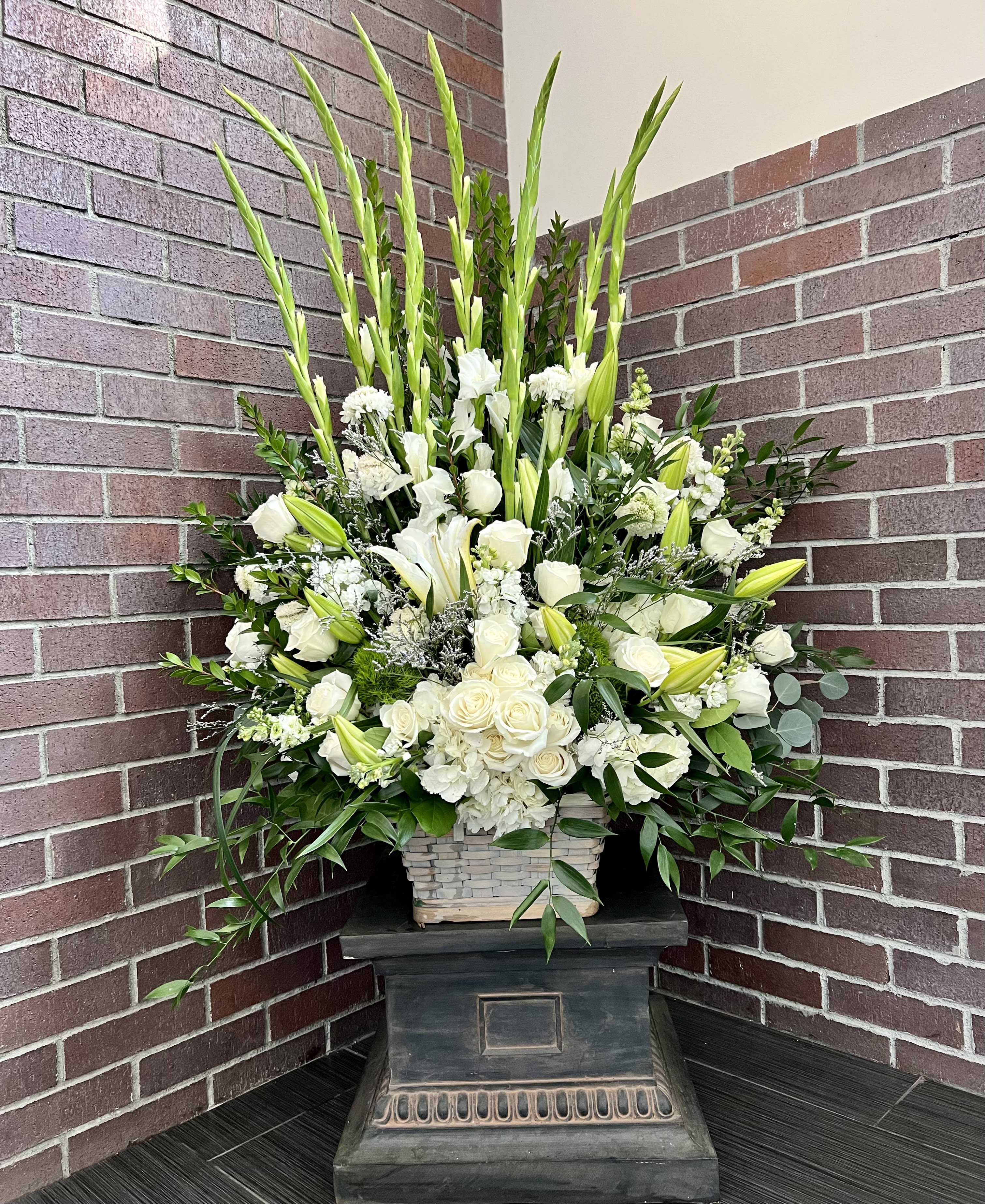 Tall white arrangement with lilies and roses in a basket on a pedestal