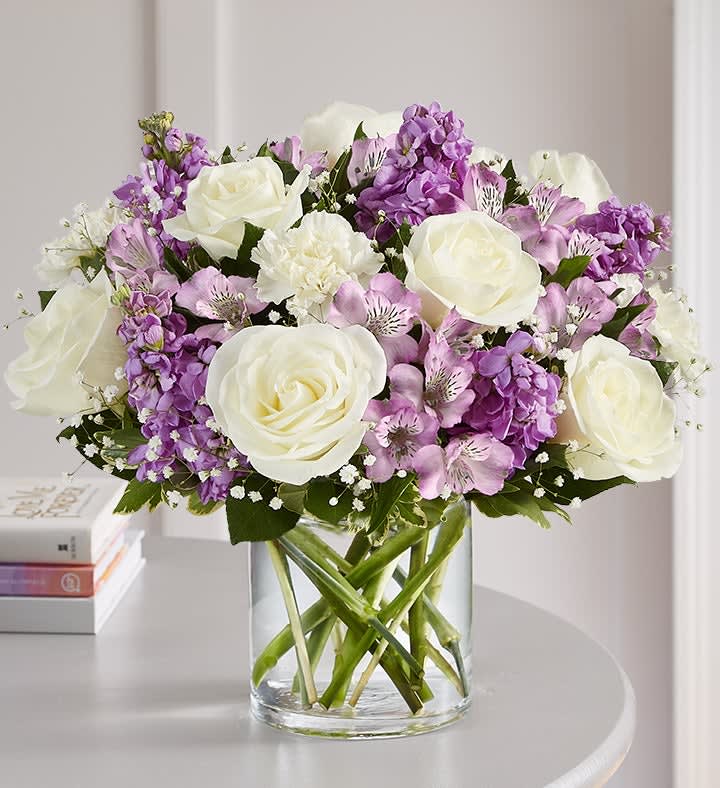 White roses and purple flowers arranged in a clear glass vase
