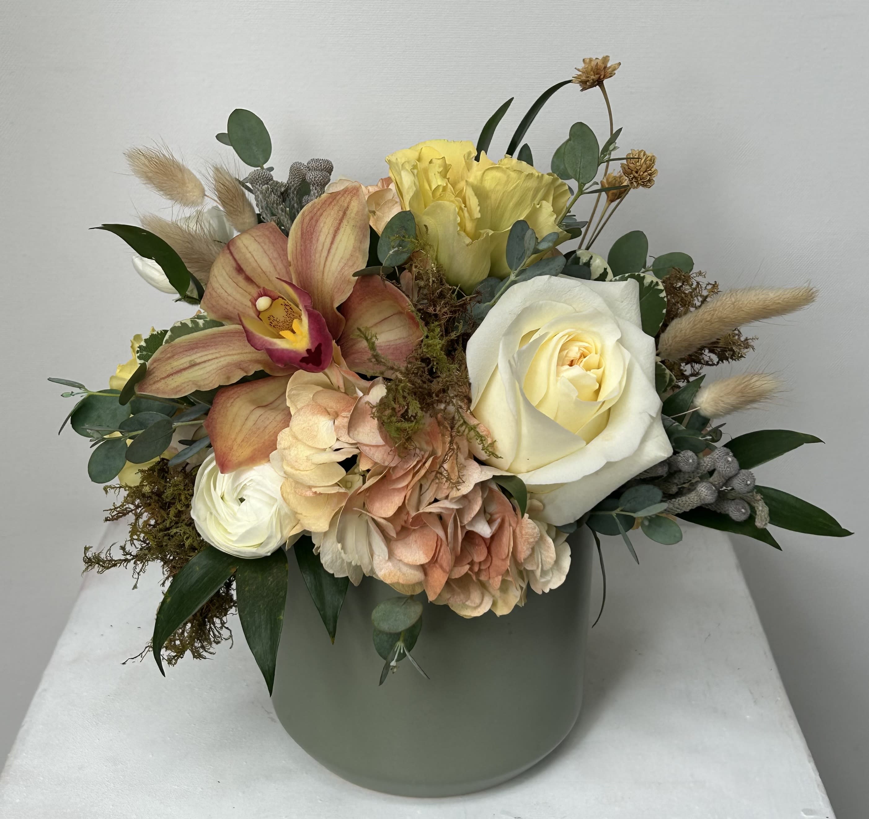 Mixed bouquet in a pale green vase with roses, orchids, hydrangea, and dried accents