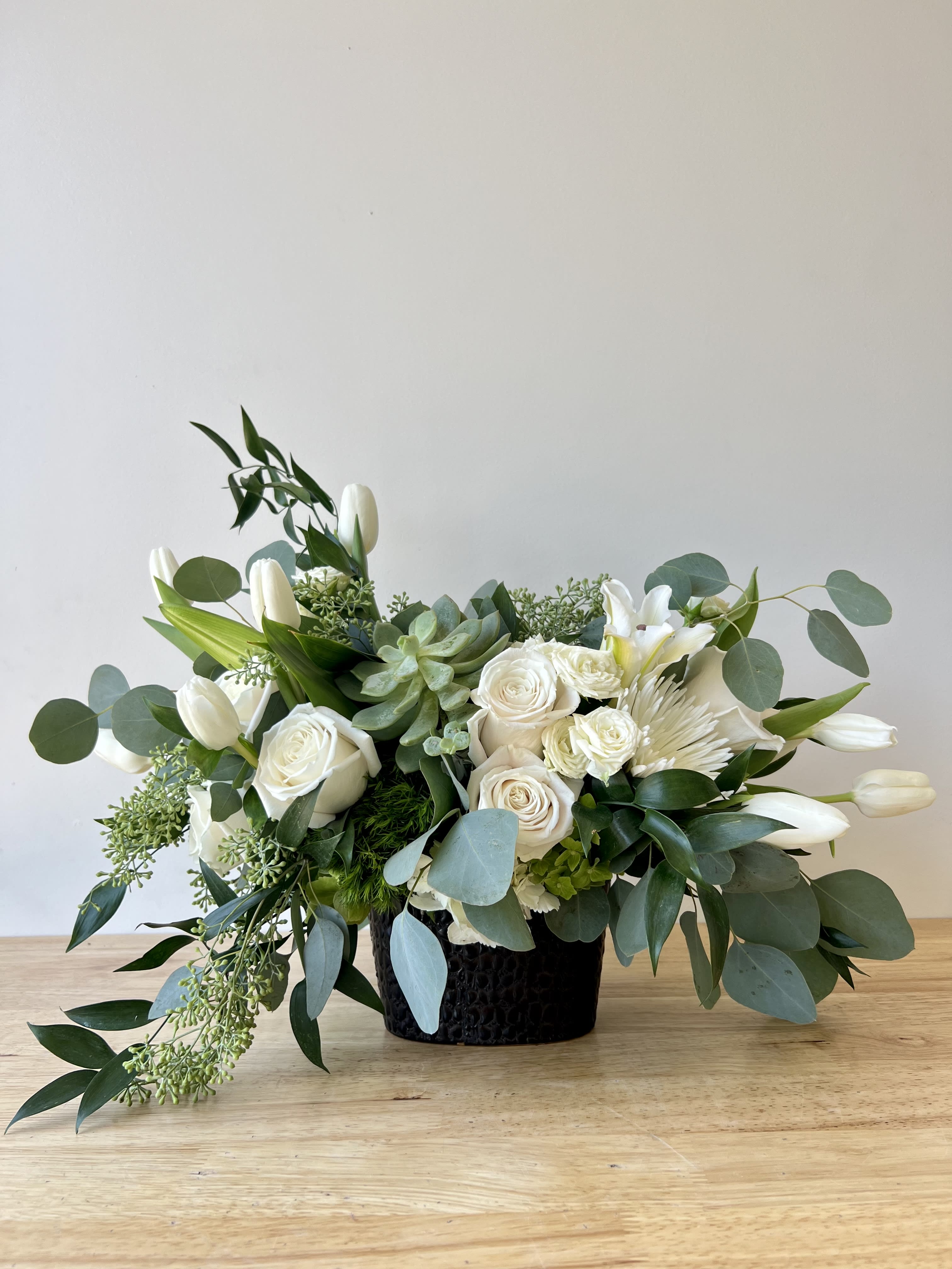 White floral arrangement in a black vase with eucalyptus and succulents