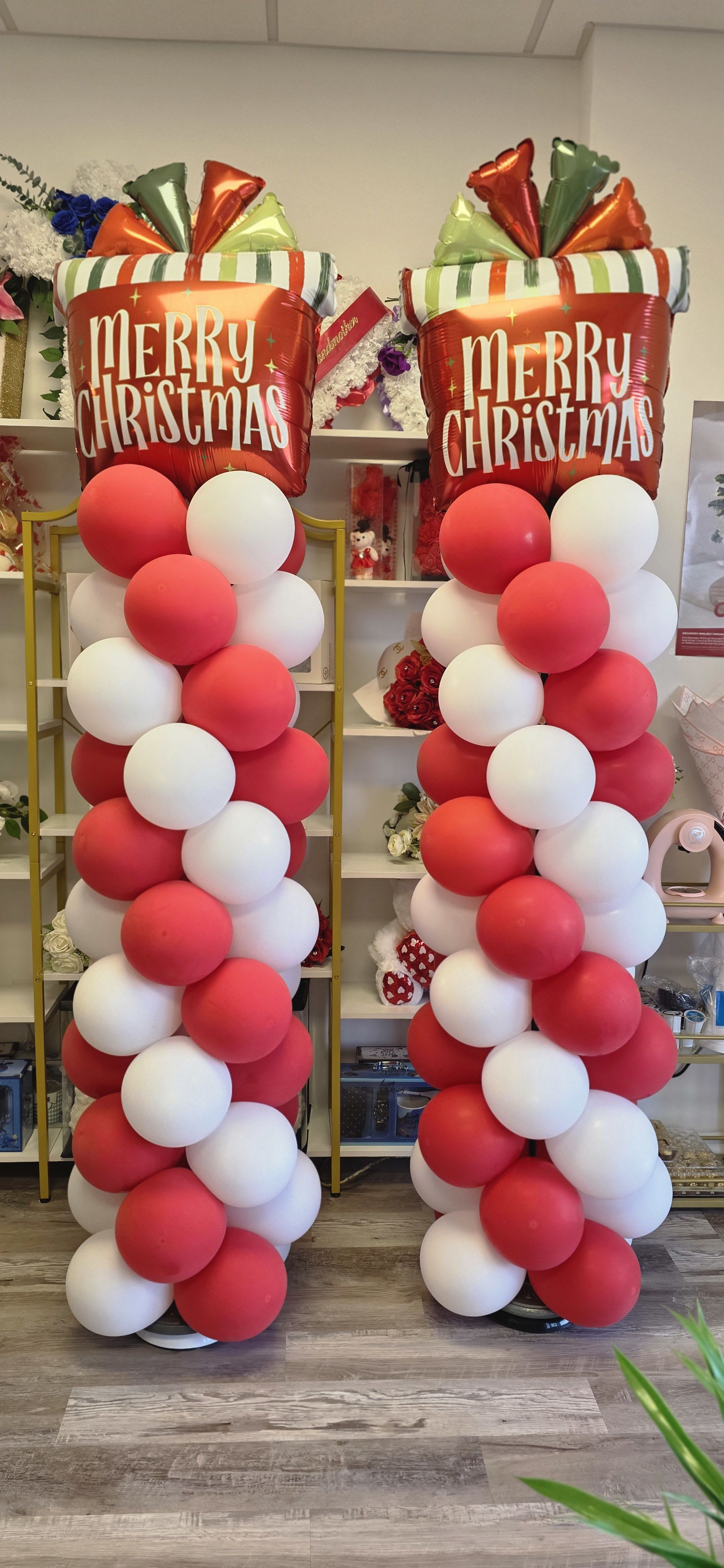 Two tall Christmas balloon columns with red and white balloons and Merry Christmas toppers