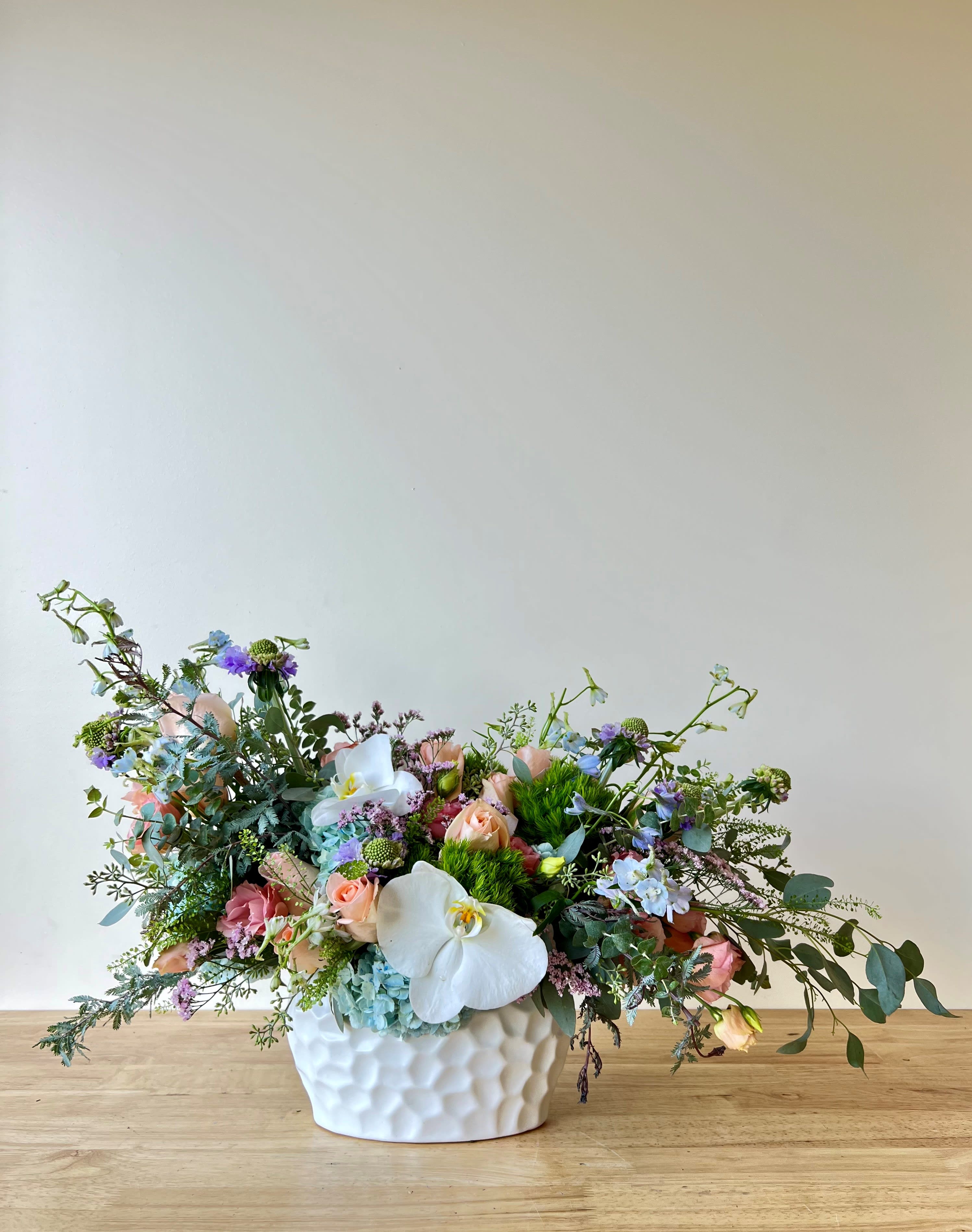 Pastel Cuddles - Beautiful one-sided arrangement with a mix of seasonal flowers like roses, hydrangeas, orchids, and more.
