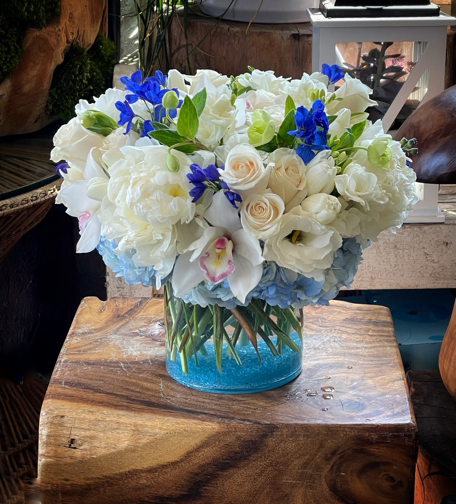 White floral arrangement with blue accents in a clear glass vase