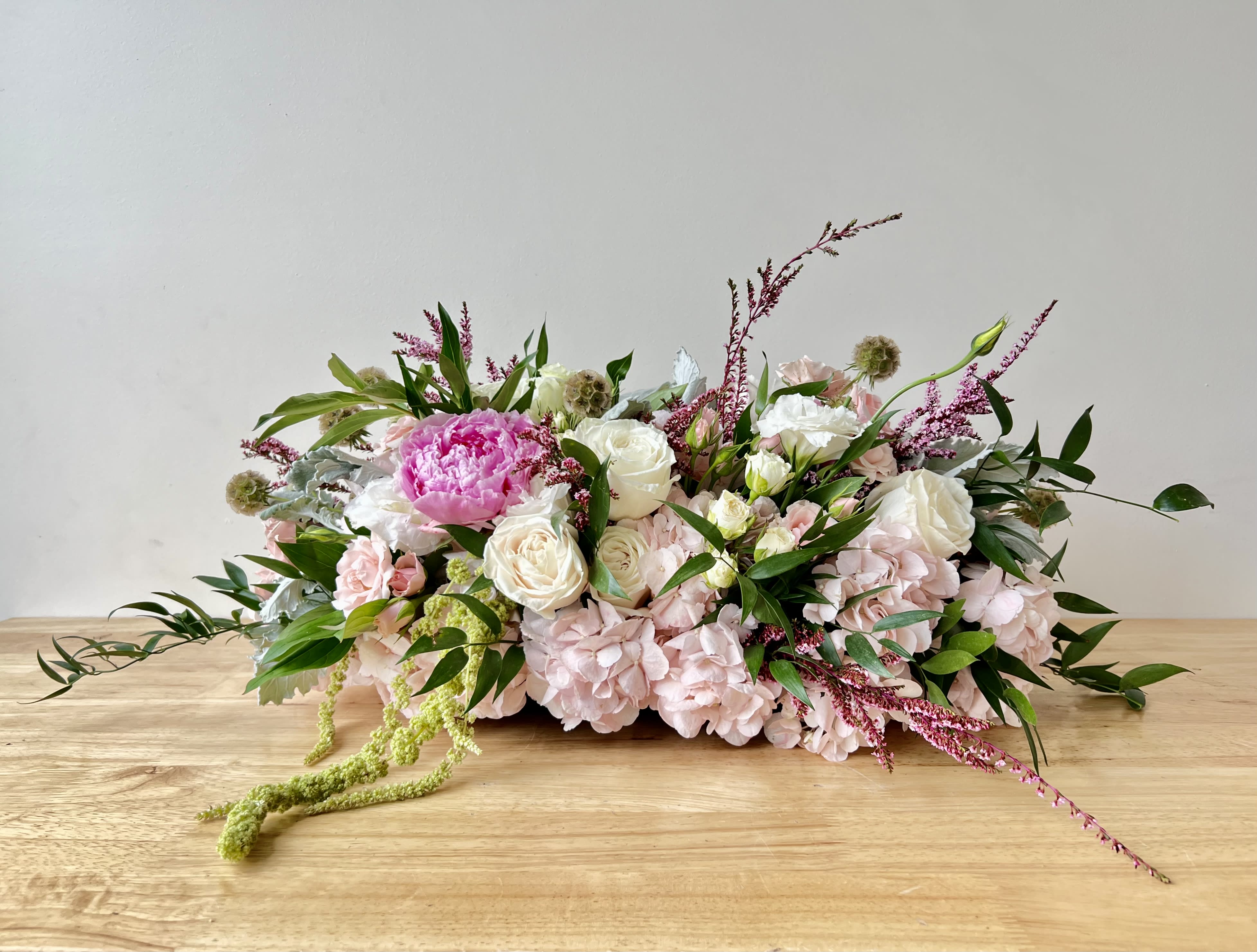 Low centerpiece of pink hydrangeas, white roses, and a bright pink peony on a wooden table