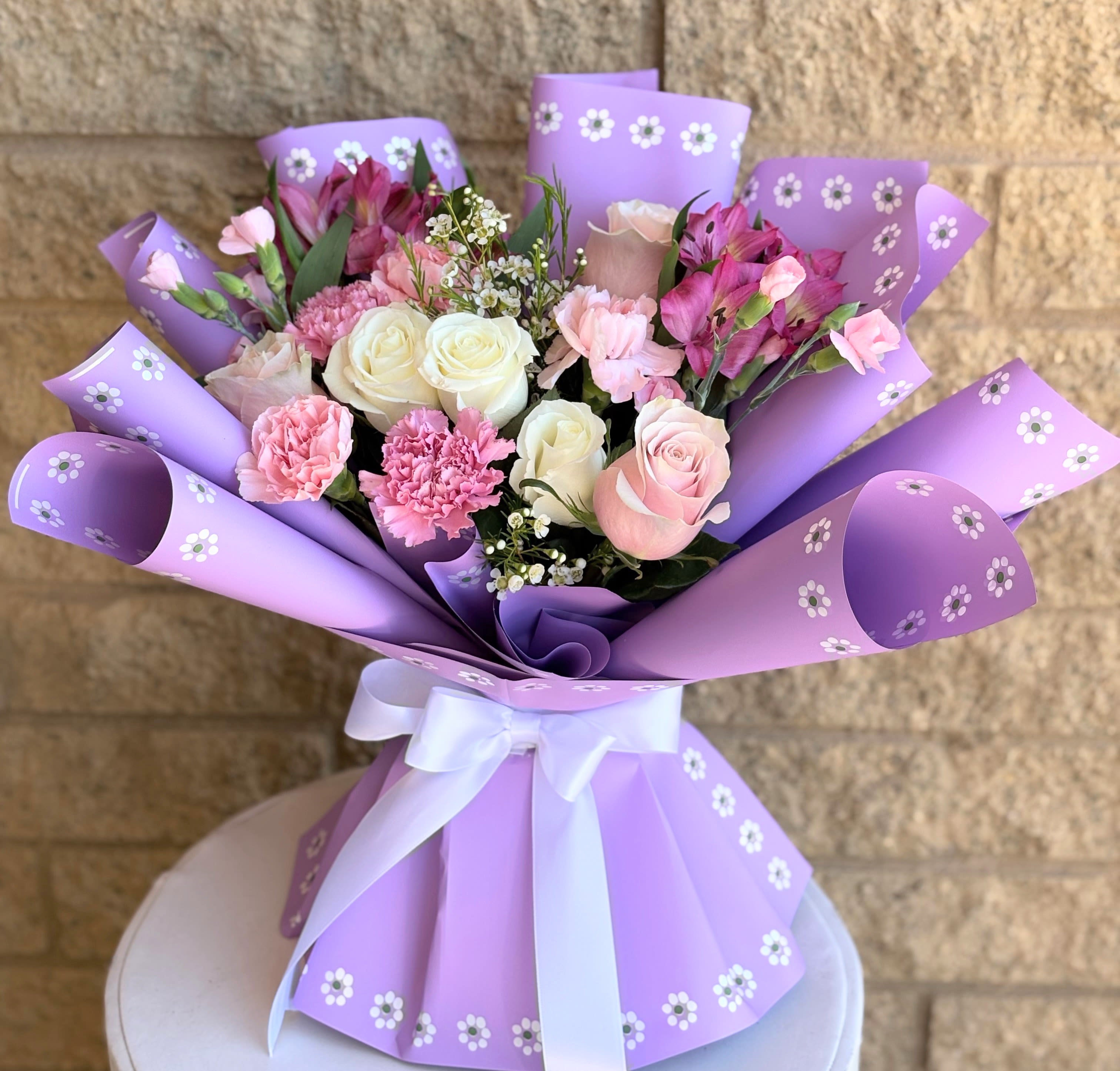 Bouquet of pink and white roses, carnations, and alstroemeria in purple wrap