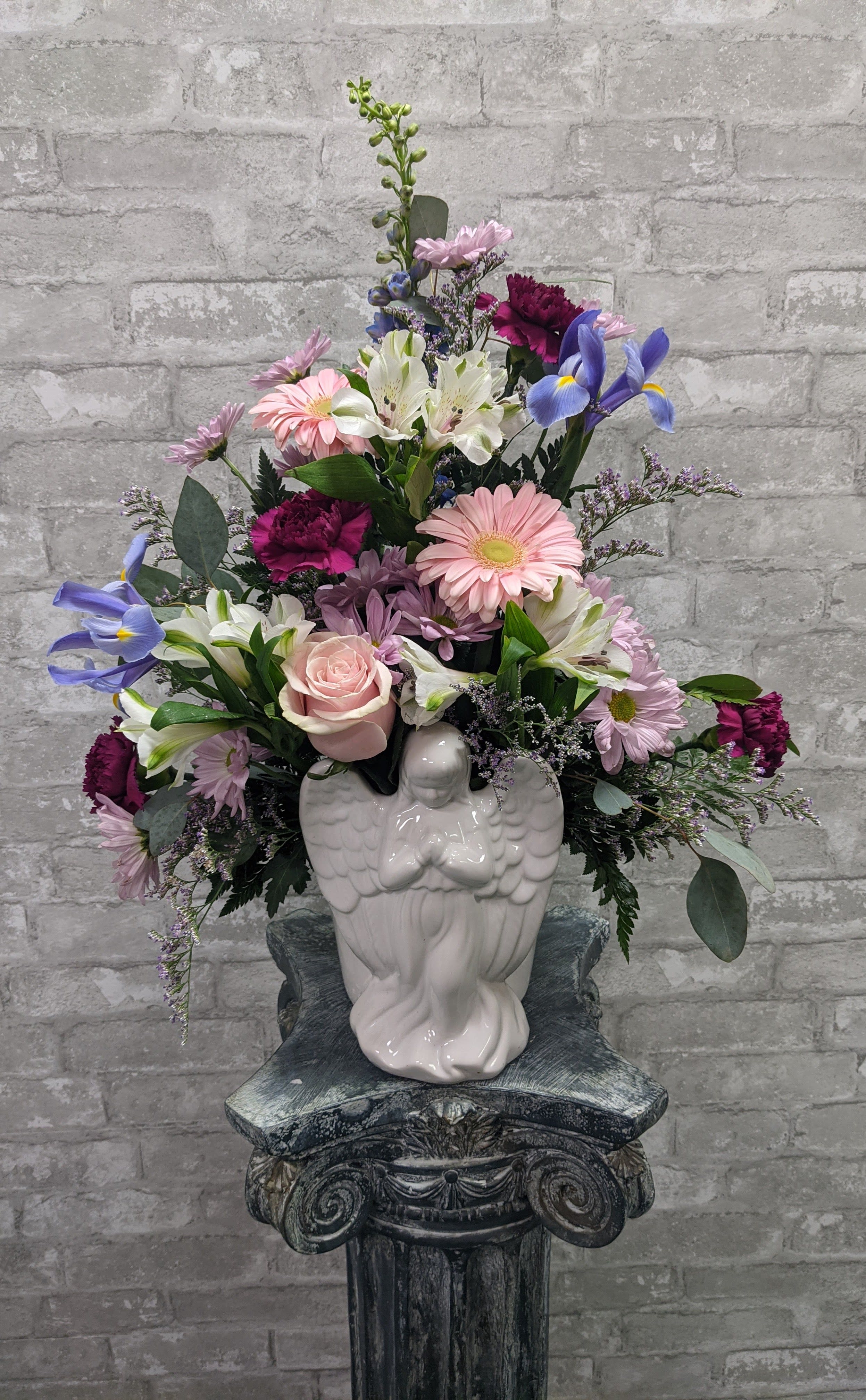 Mixed bouquet in a white angel vase with pink, white, purple, and blue flowers