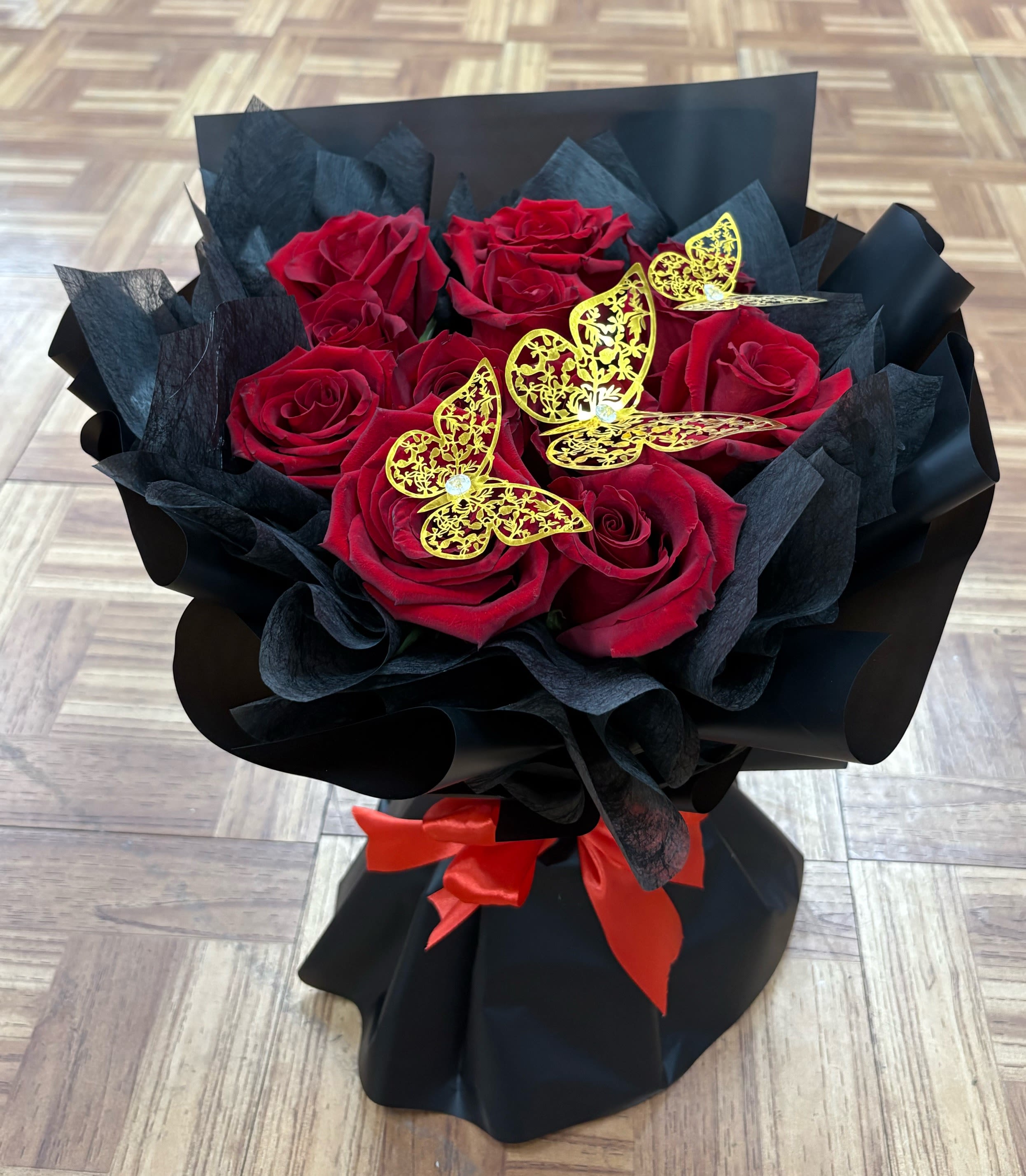 Bouquet of red roses wrapped in black paper with gold butterfly accents