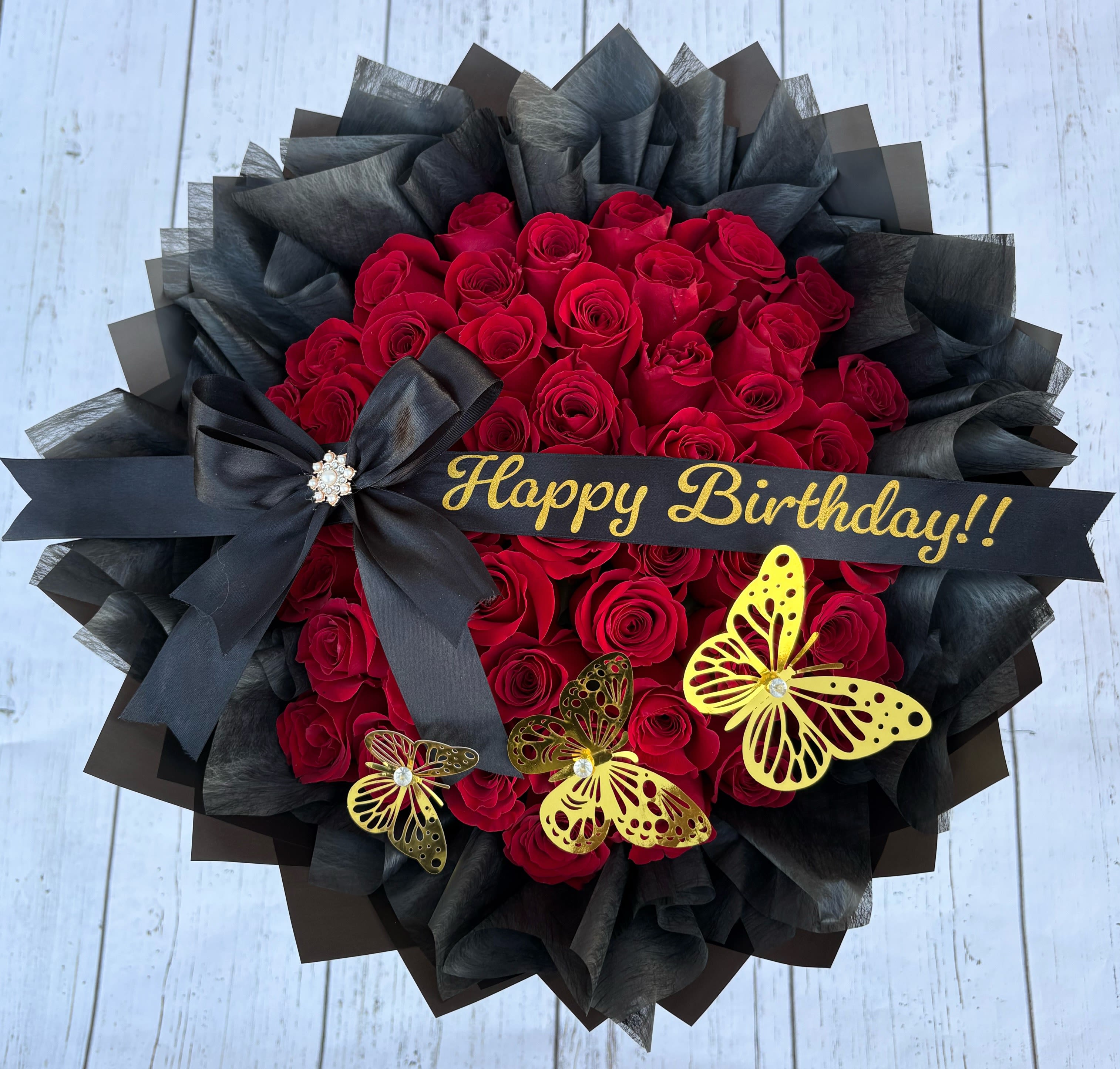 Red rose bouquet with black wrapping, a birthday ribbon, and butterfly decorations