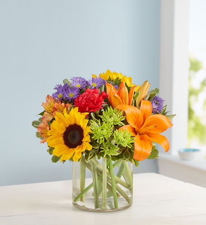 Mixed bouquet with sunflowers, lilies, and purple daisies in a glass vase