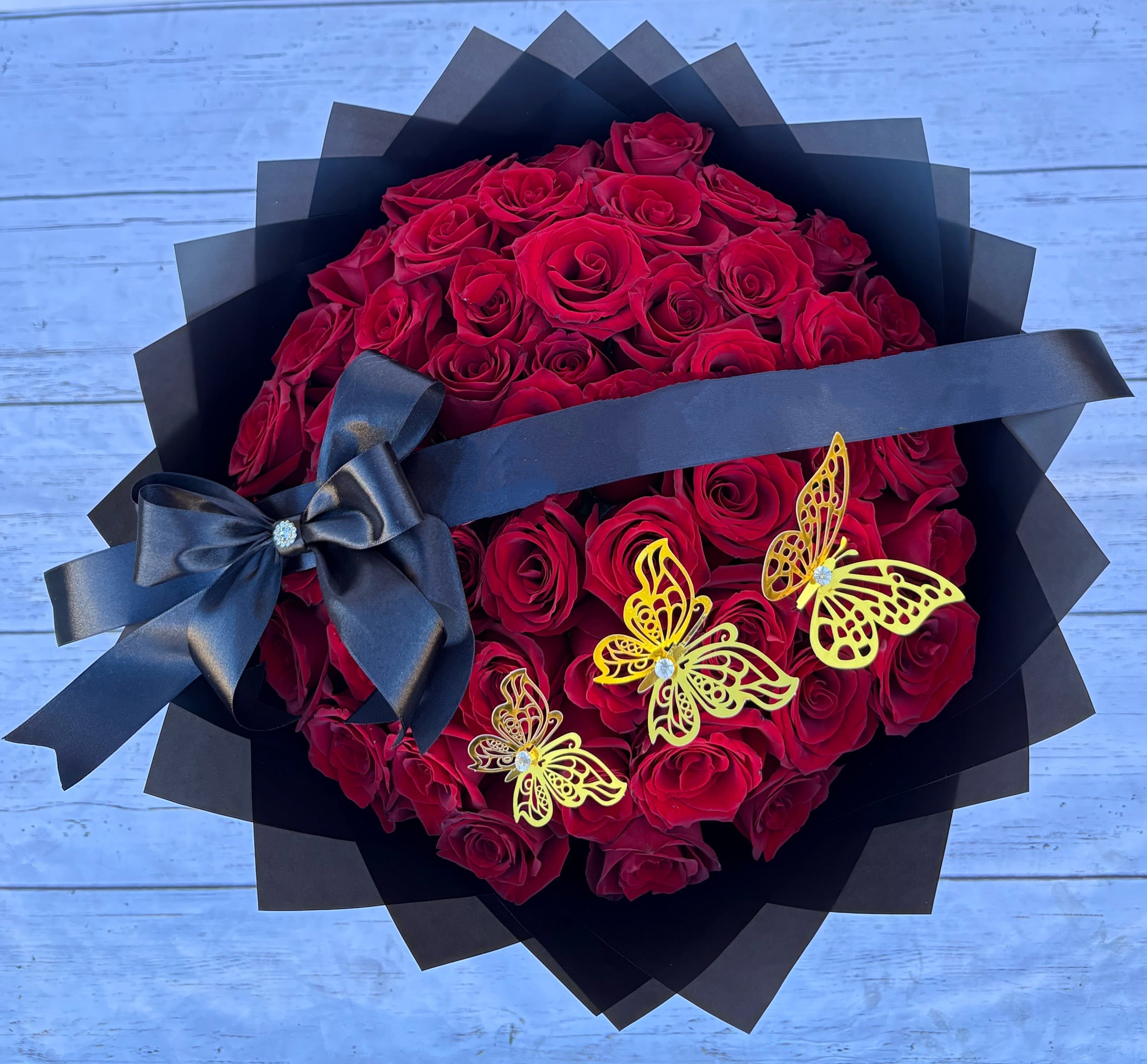 Bouquet of red roses wrapped in black paper with a black ribbon and butterfly accents
